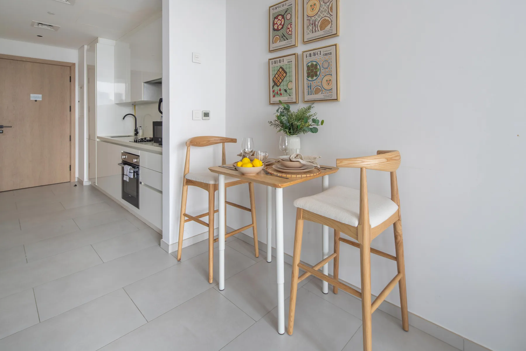 Una pequeña zona de comedor con mesa y asientos de madera junto a una cocina compacta.