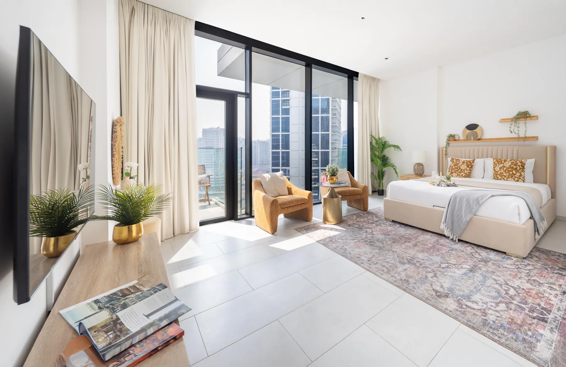 A bright bedroom with a bed, seating, and floor-to-ceiling windows.