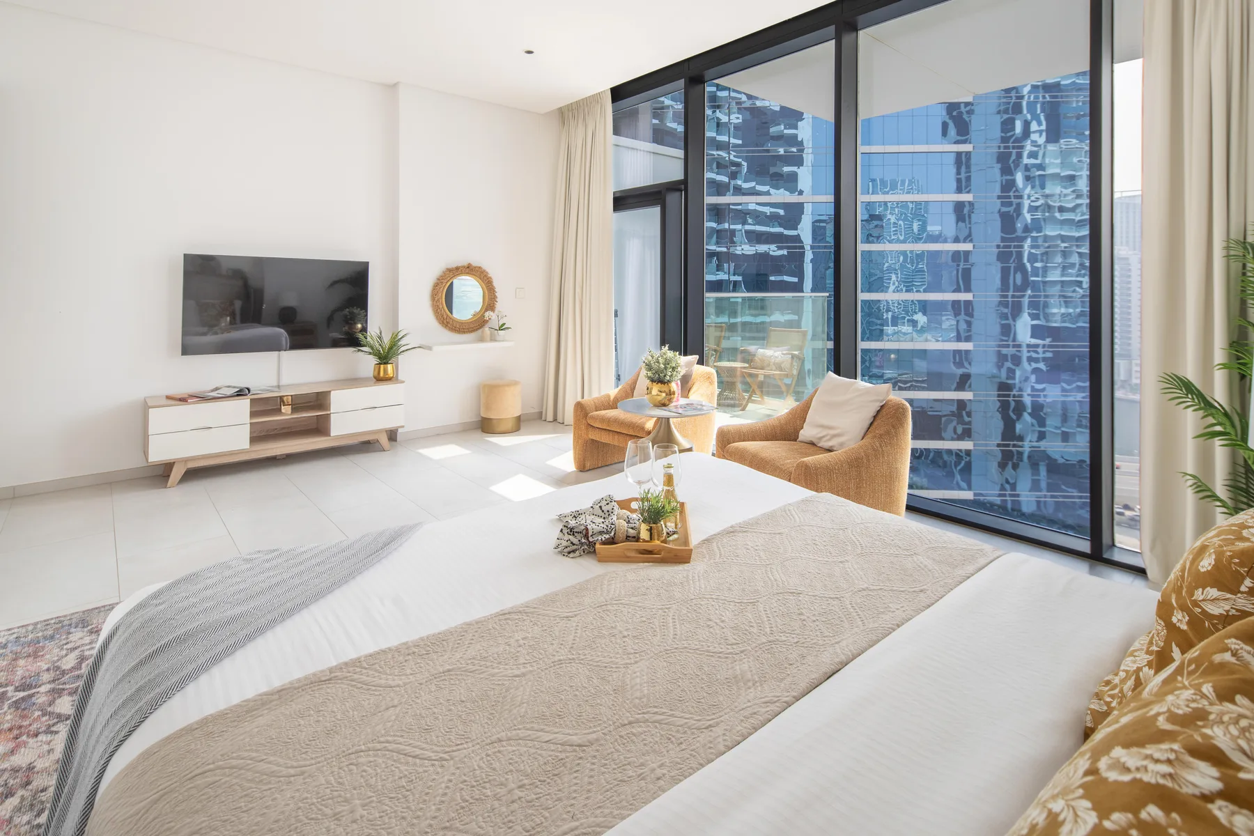 Un dormitorio luminoso con cama, zona de estar y ventanales.