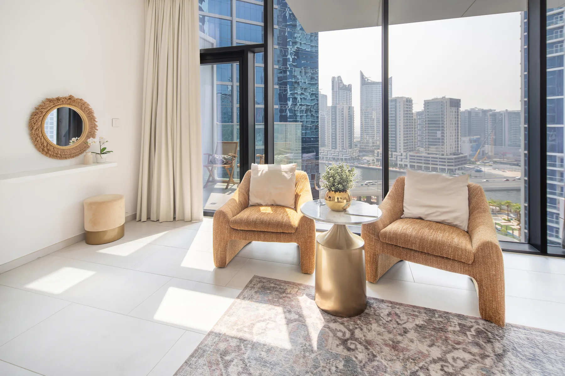 A bright living area with two woven seats beside floor-to-ceiling windows overlooking city buildings.