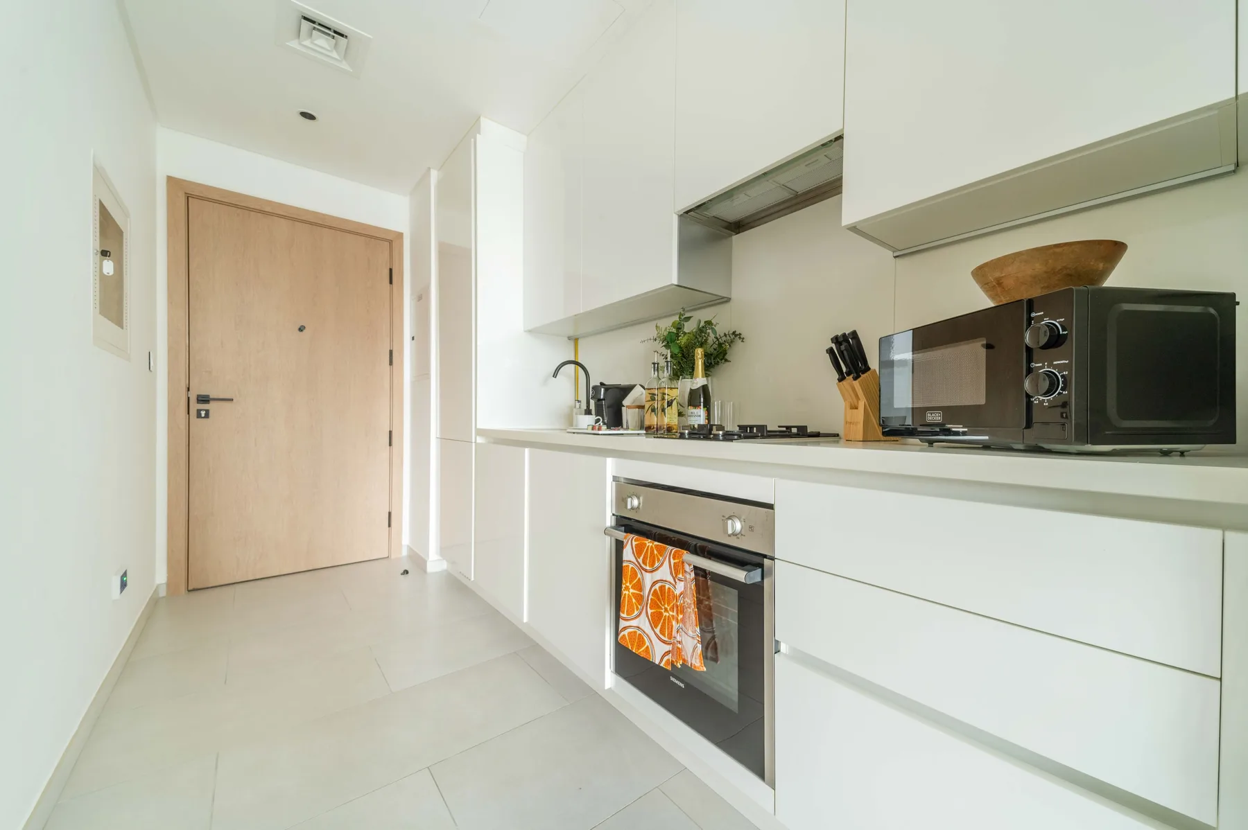 Una cocina compacta con armarios blancos, una placa de cocina y un horno integrado.