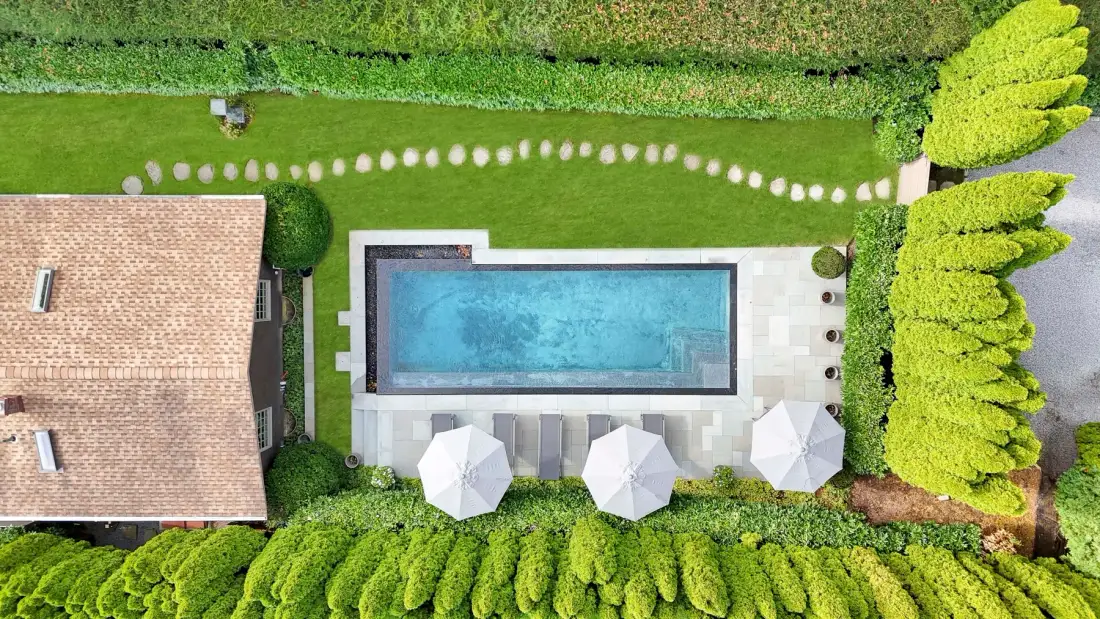An aerial view shows a rectangular swimming pool beside a house and landscaped garden.