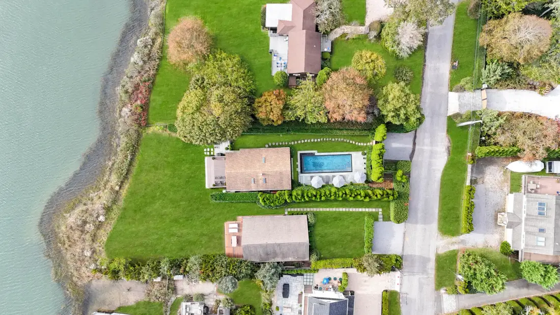 An aerial view of lakeside homes, lawns, and a swimming pool.
