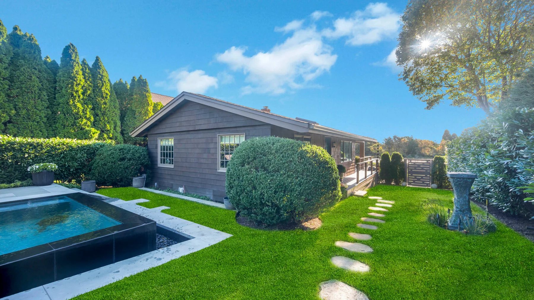 A garden surrounds a house and swimming pool, with stepping stones across the lawn.