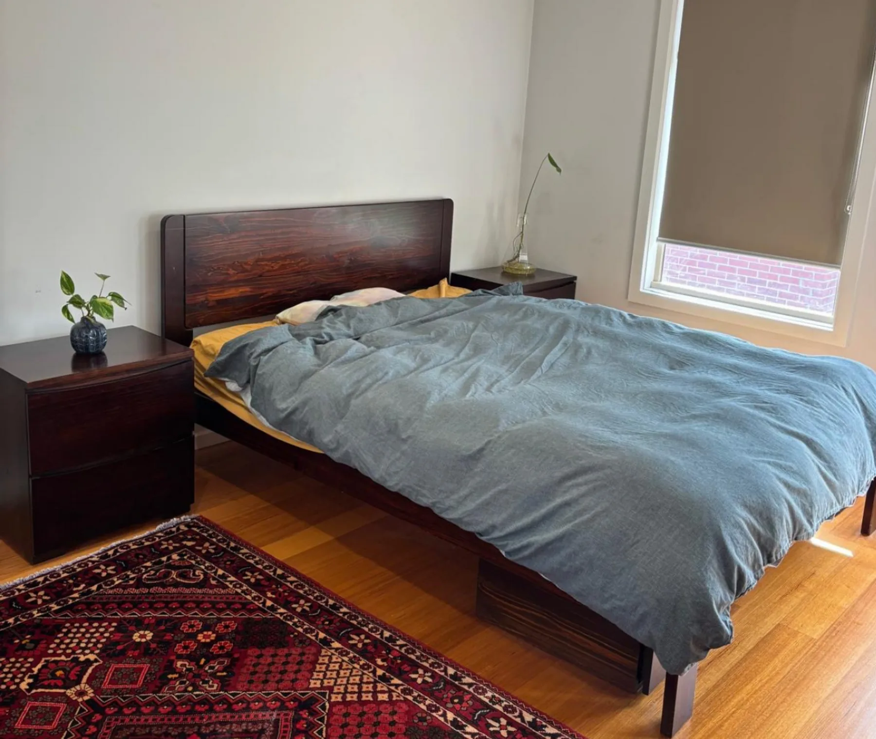 A bedroom with a bed covered by a gray blanket beside a window.