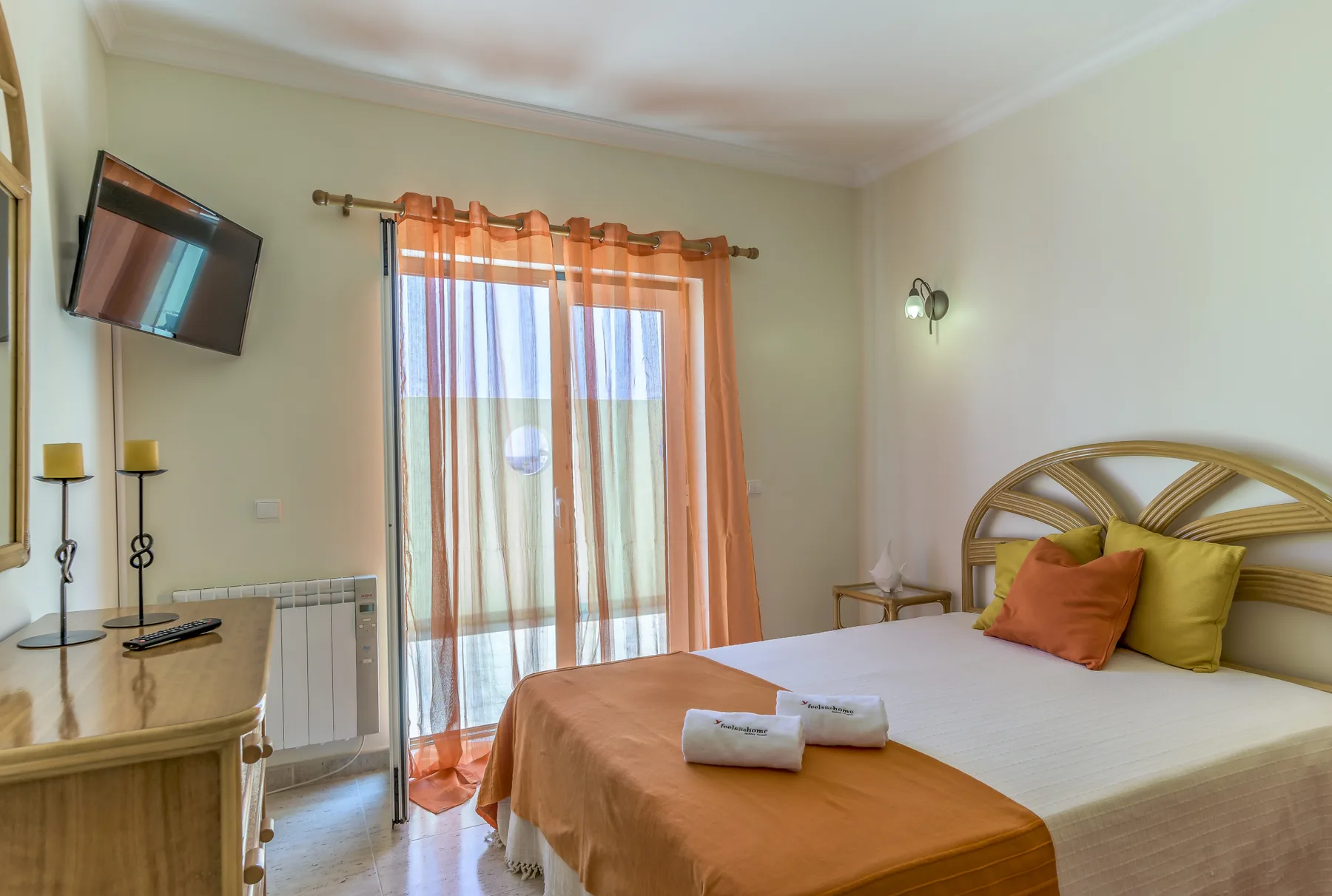 Dormitorio con una cama, cortinas naranjas y un televisor en la pared.