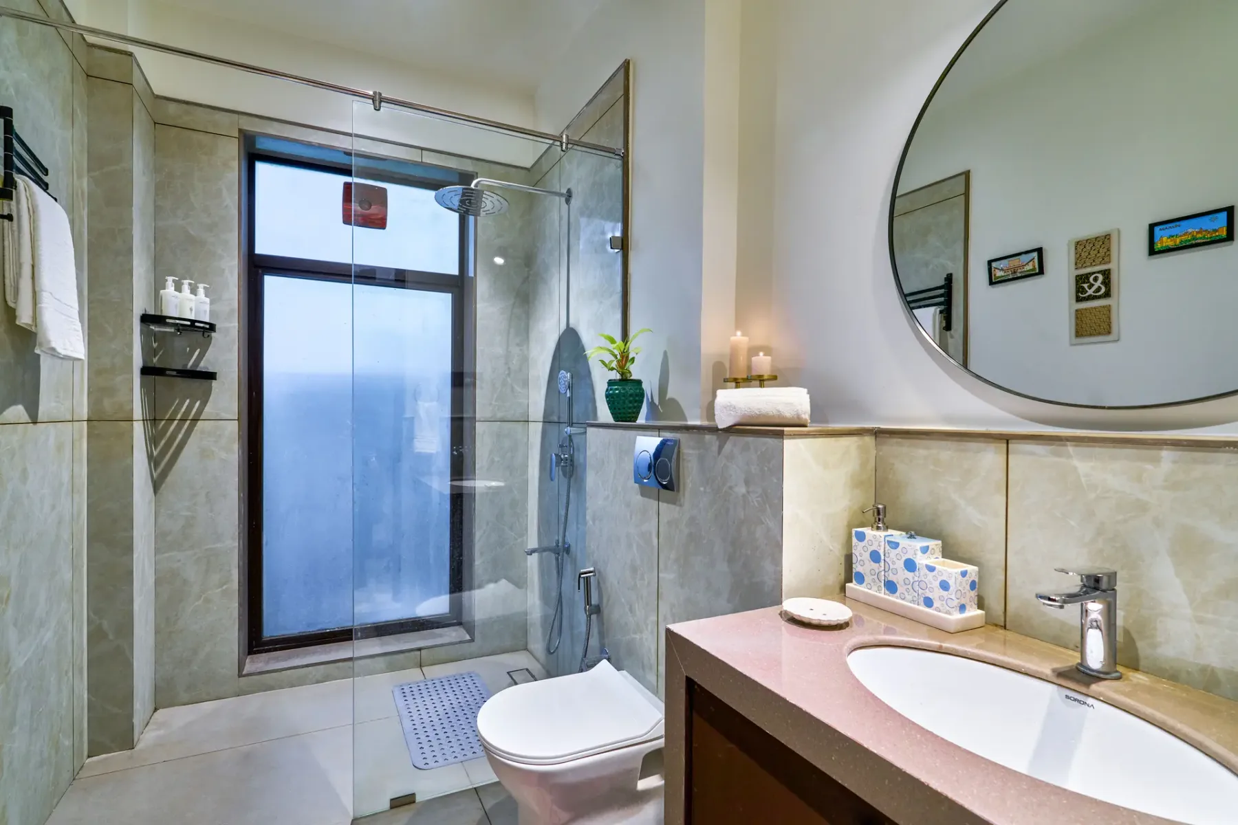 A bathroom with a glass shower, toilet, and sink beneath a large round mirror.