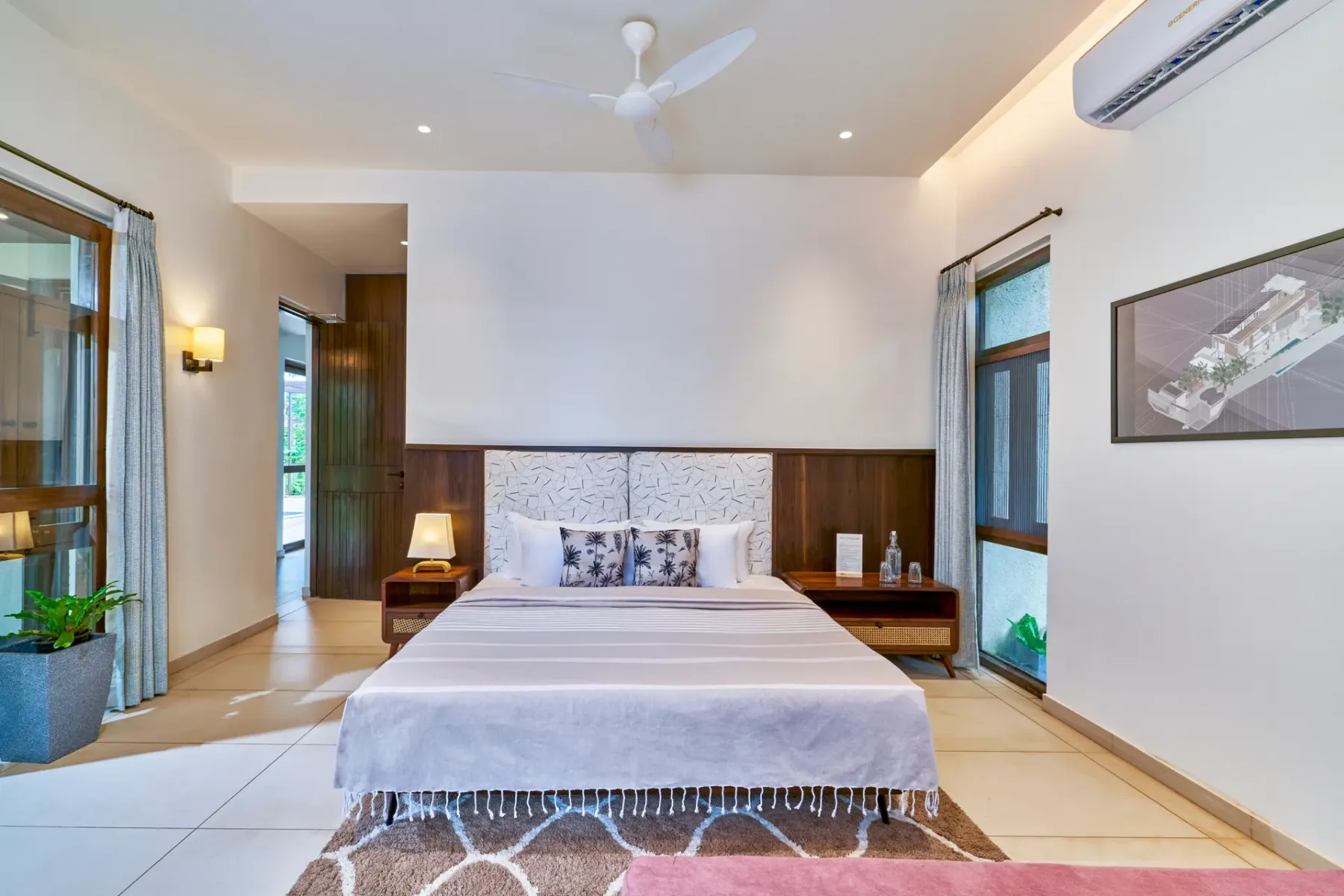 A bedroom with a neatly made bed, bedside tables, and windows on either side.