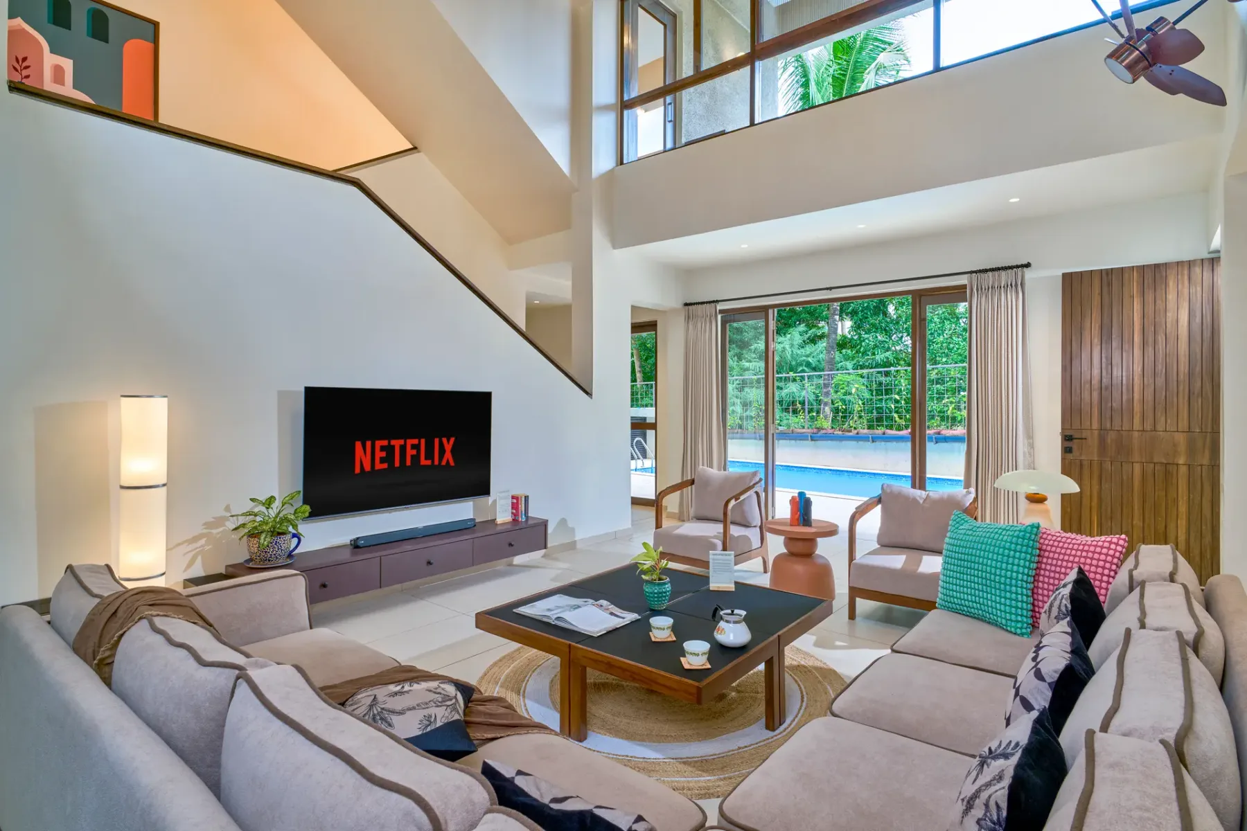 A bright living room with seating around a coffee table and windows overlooking a pool.