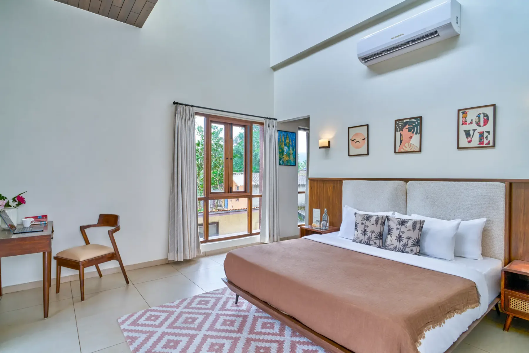 A bright bedroom with a large bed, framed artwork, and a glass door opening to greenery.