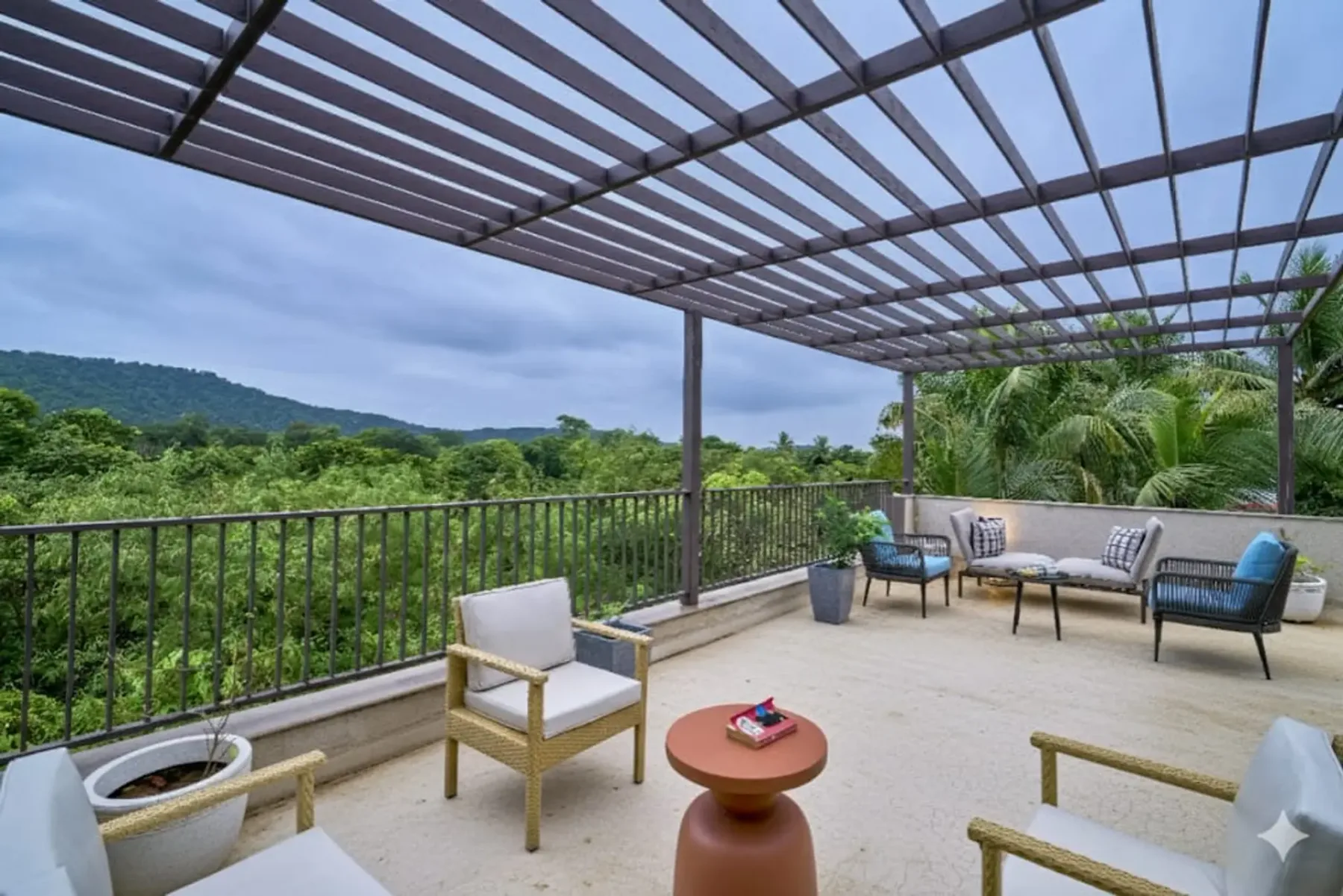 A covered outdoor terrace with seating overlooks a green, tree-covered landscape.