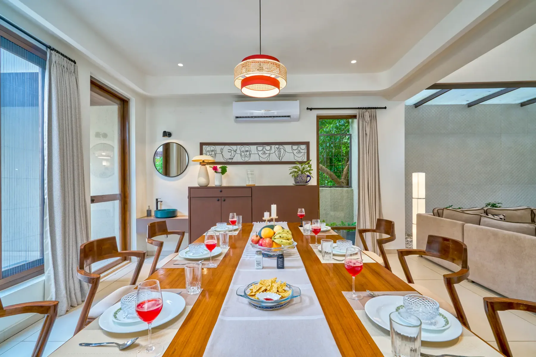A dining area with a long wooden table set for a meal beside a living area.