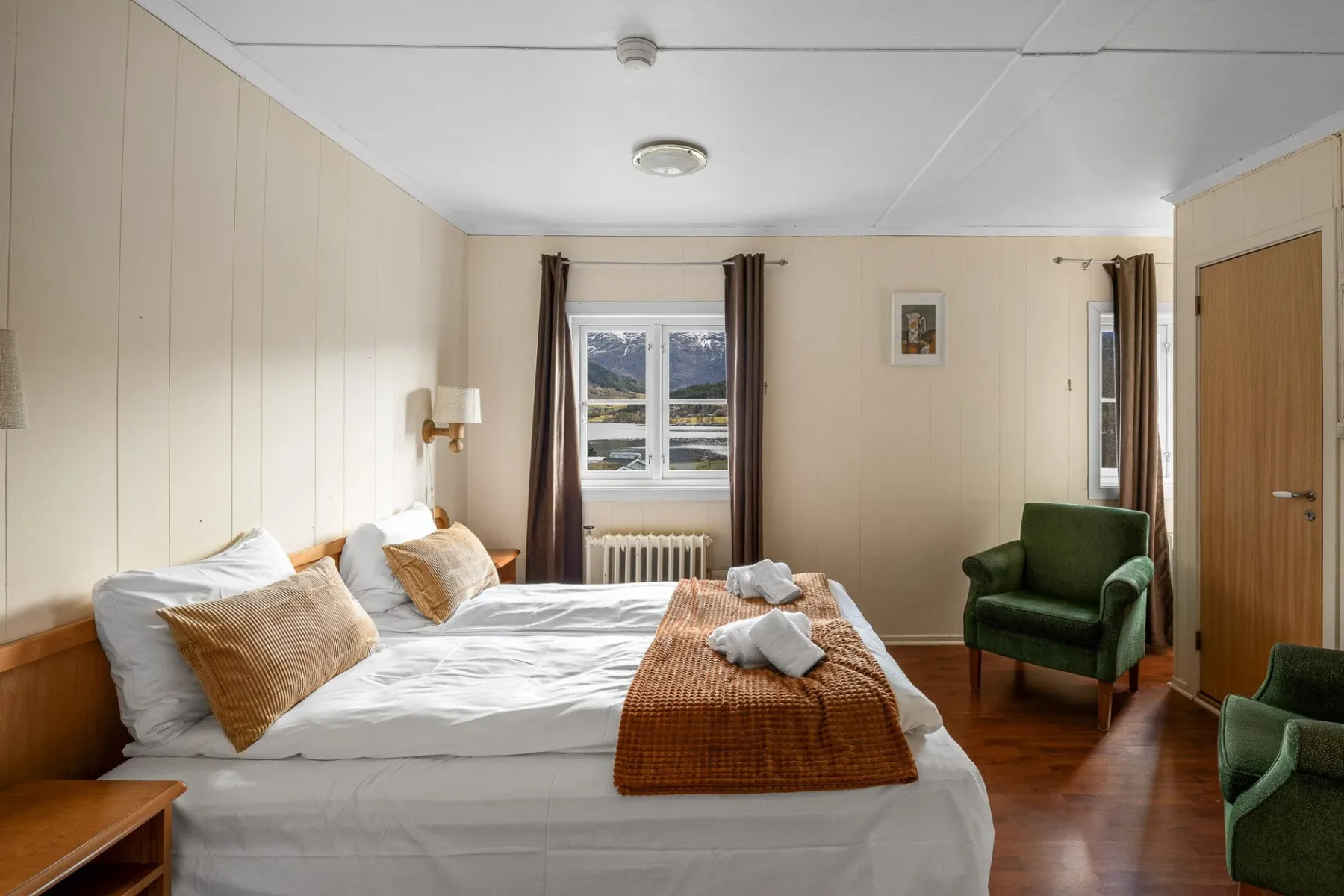Bedroom with a large bed, green chairs and wood paneling.