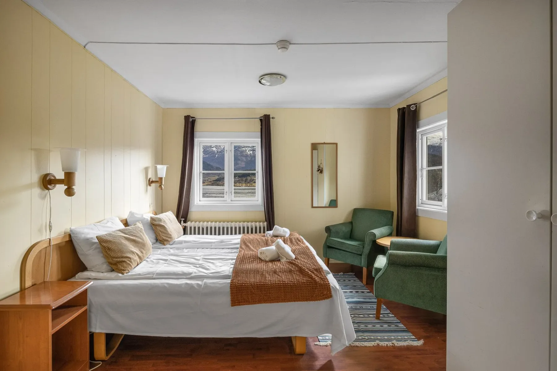 Bedroom with a bed, green chairs and windows.