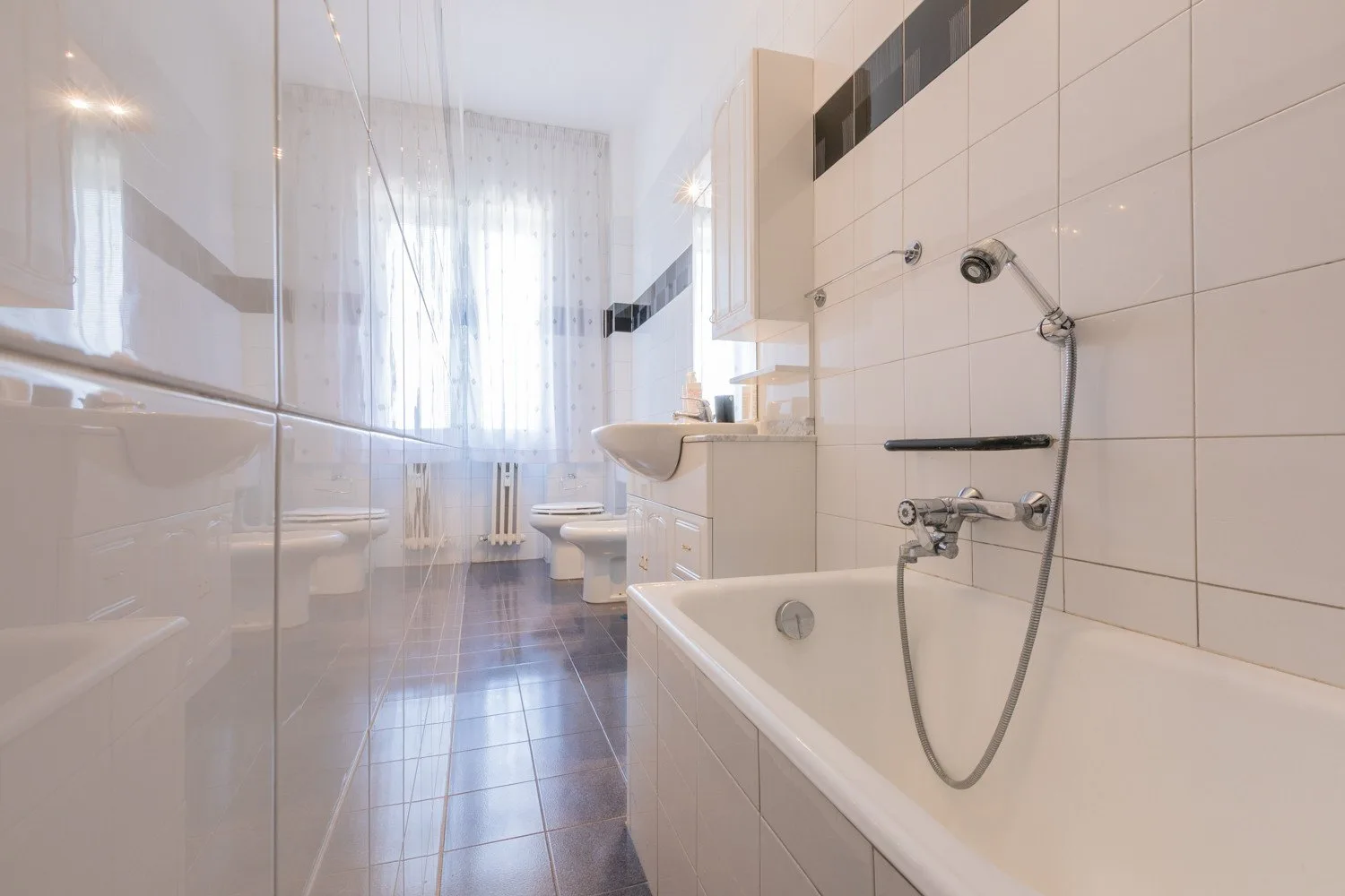 A tiled bathroom with a bathtub and shower beside a curtained window.
