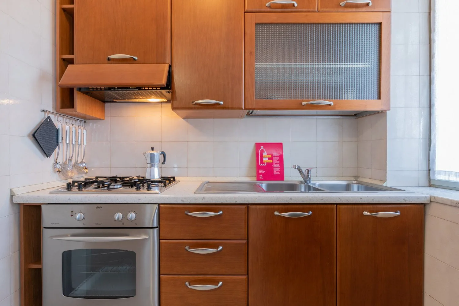 A kitchen with wooden cabinets, a cooktop, oven, and sink.