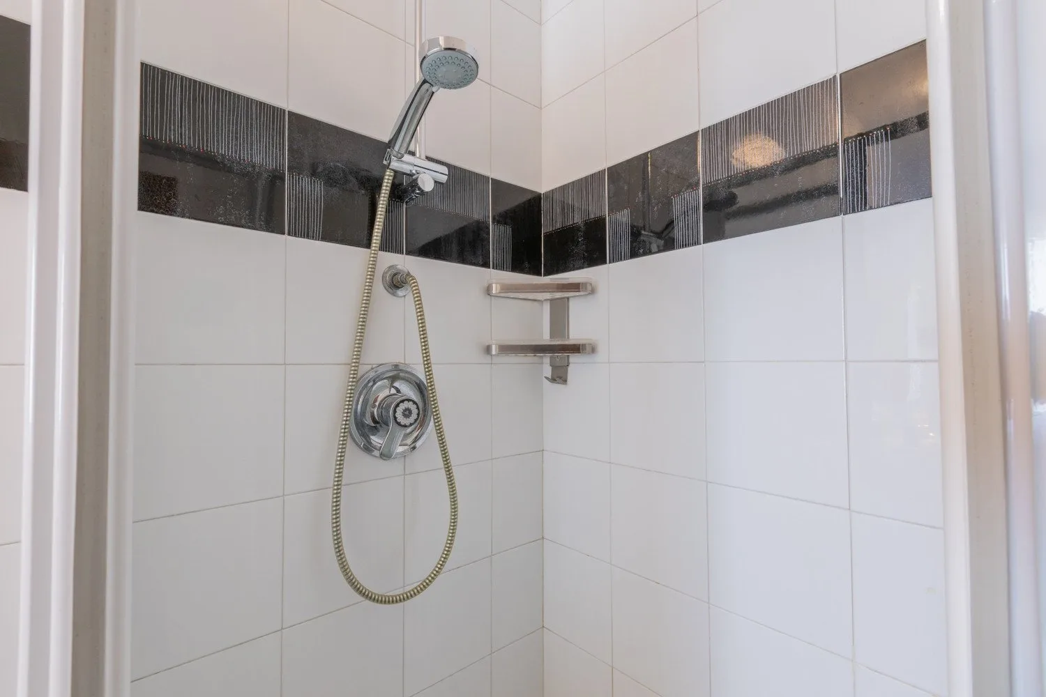 A tiled shower with a handheld showerhead and wall-mounted shelves.
