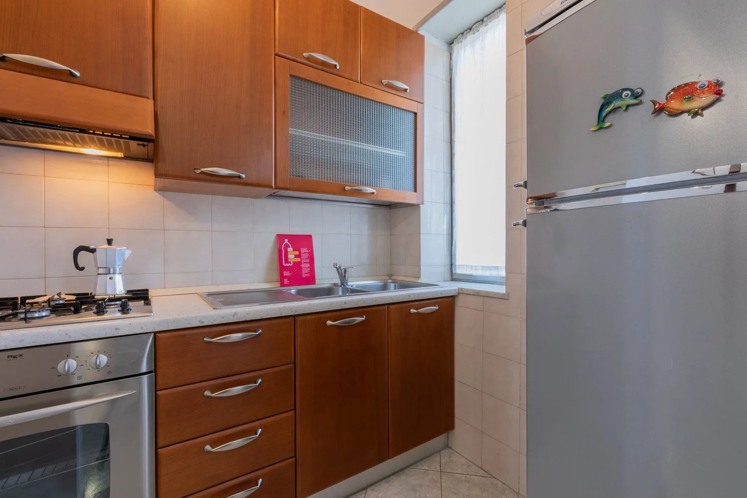 A compact kitchen with wooden cabinets, a stovetop, and a sink beside a window.