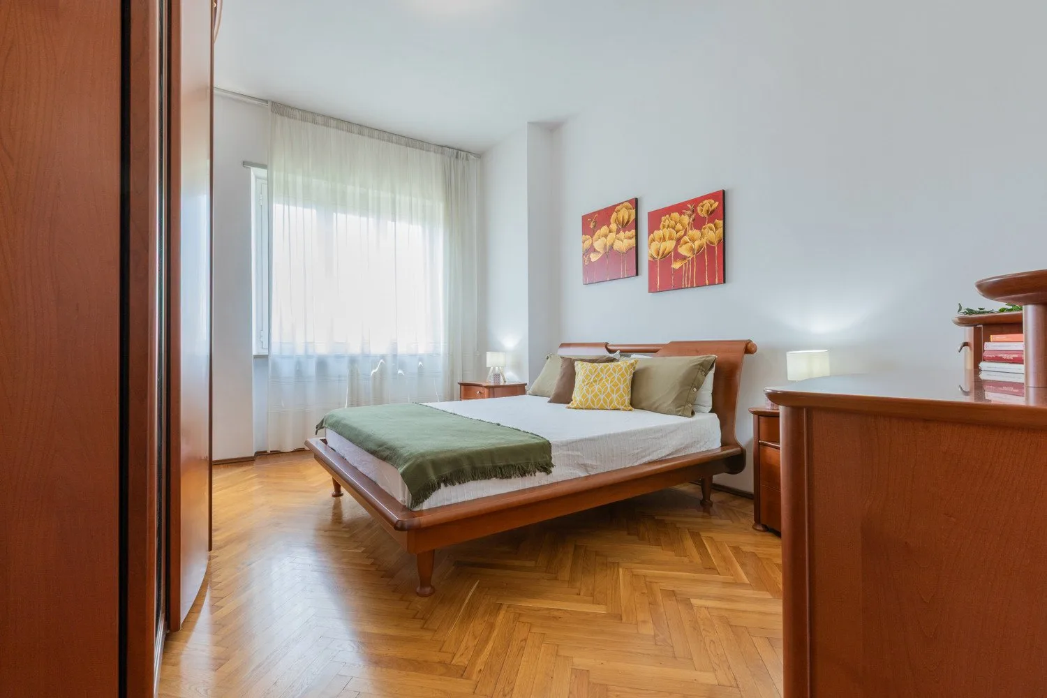 A bedroom with a wooden bed, green bedding, and a bright curtained window.