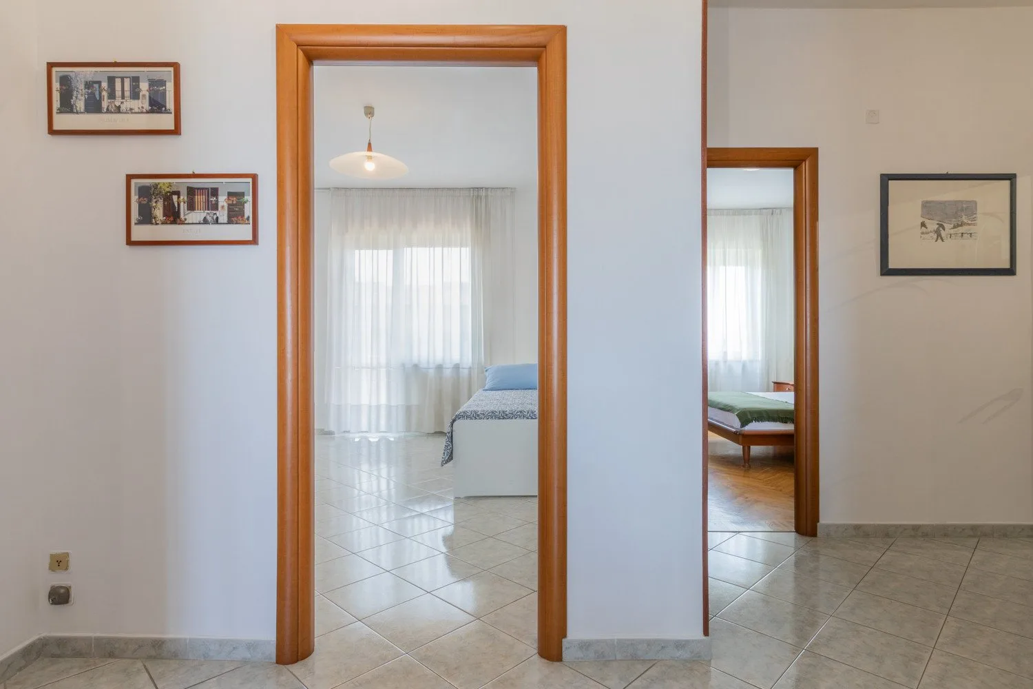A bright interior hallway opens onto rooms with tiled floors and framed wall art.