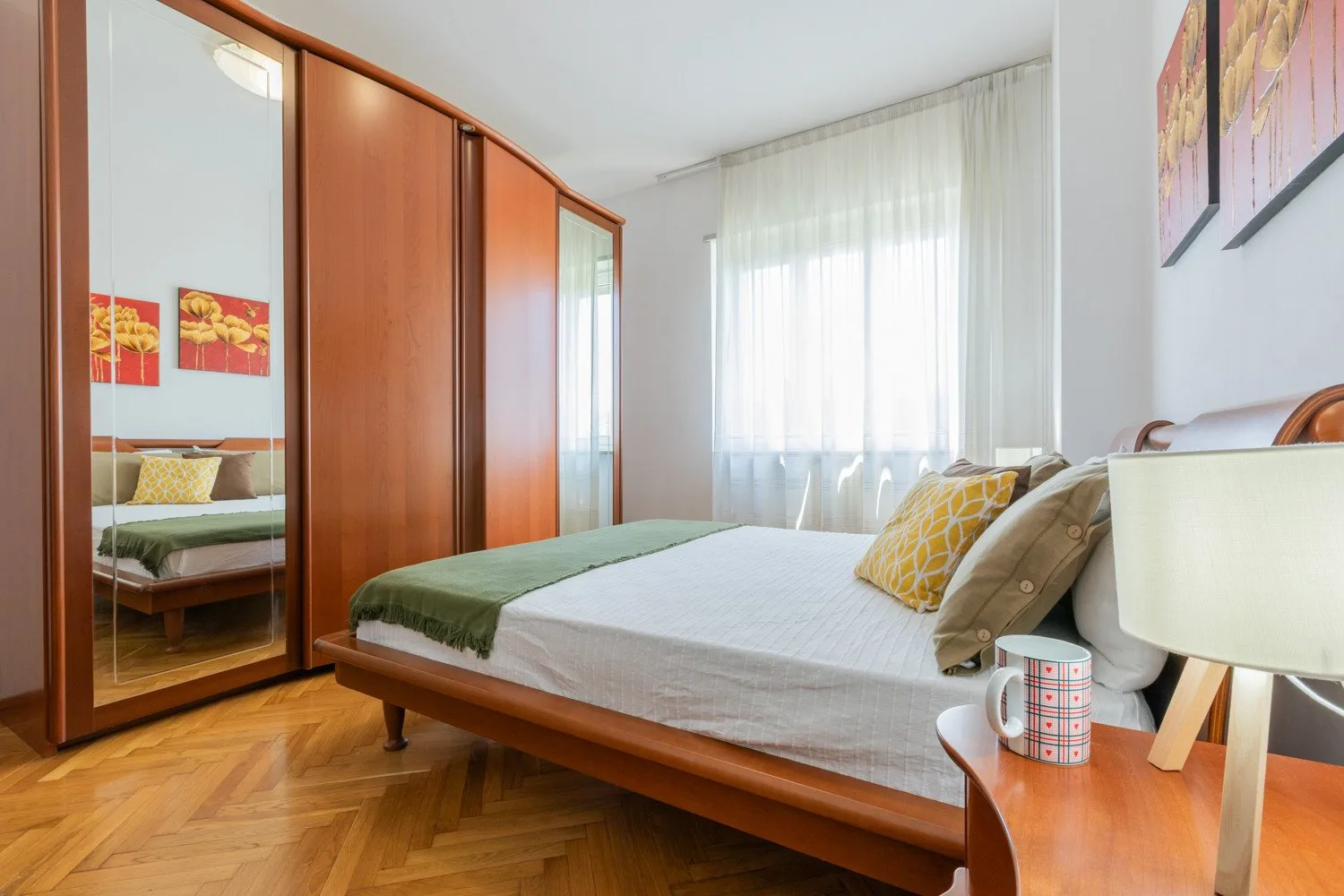 A bedroom with a low bed, mirrored wardrobe, and sheer curtains.