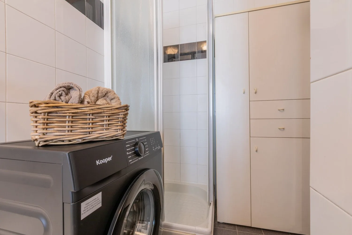 A tiled laundry and shower area with a washing machine and storage cabinet.