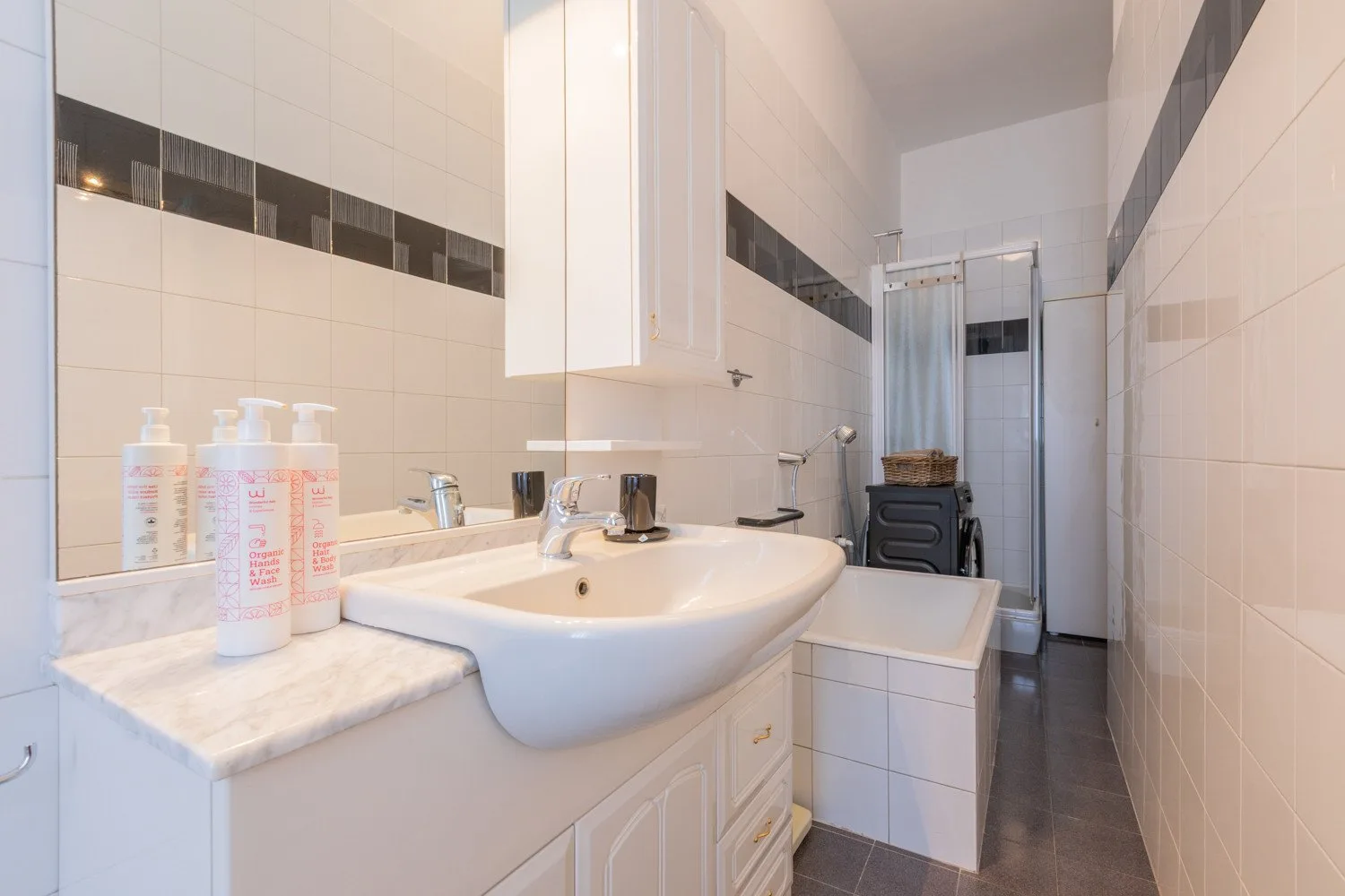 A tiled bathroom with a wide sink and a shower at the far end.