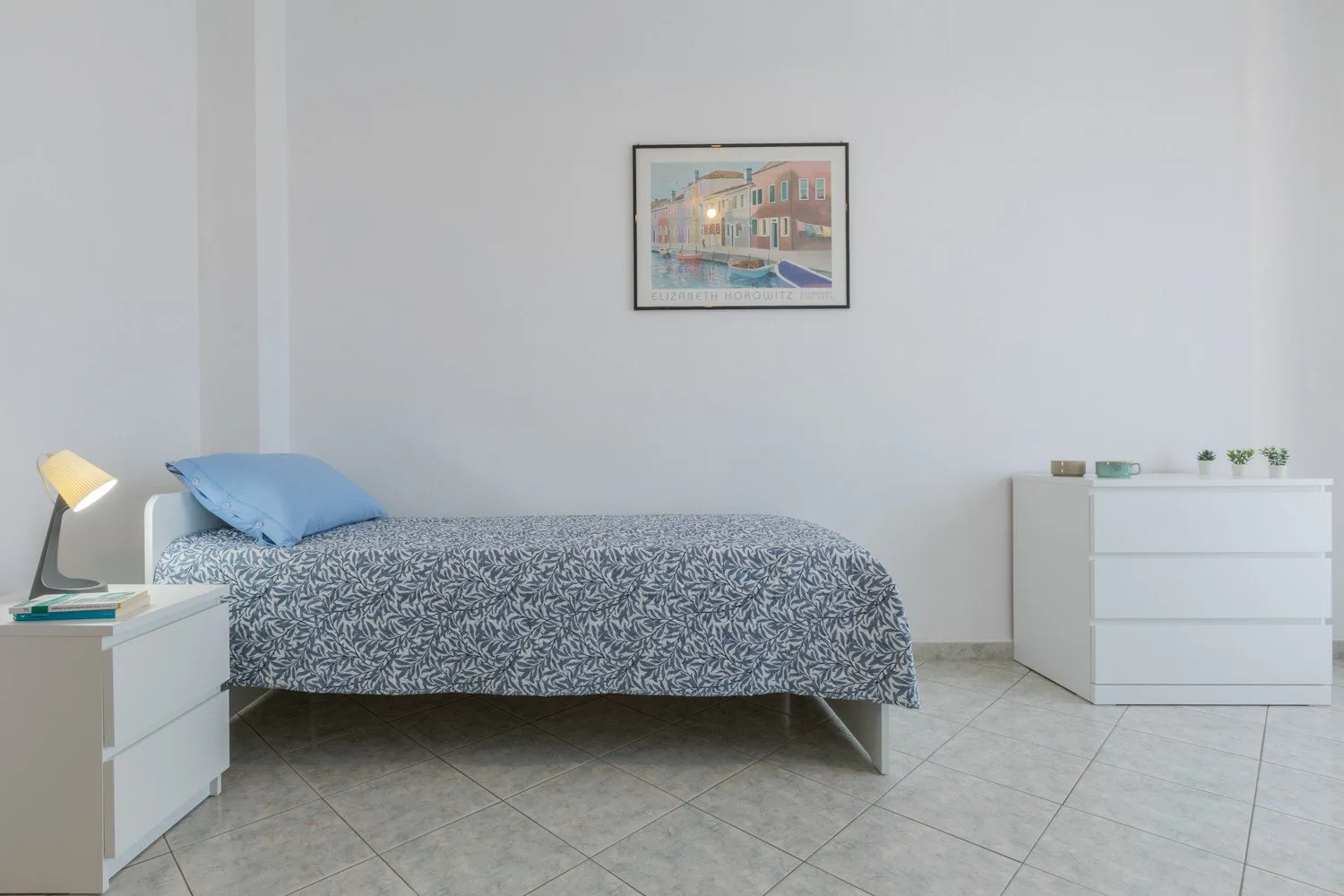 A bedroom with a bed, bedside table, and framed artwork on the wall.