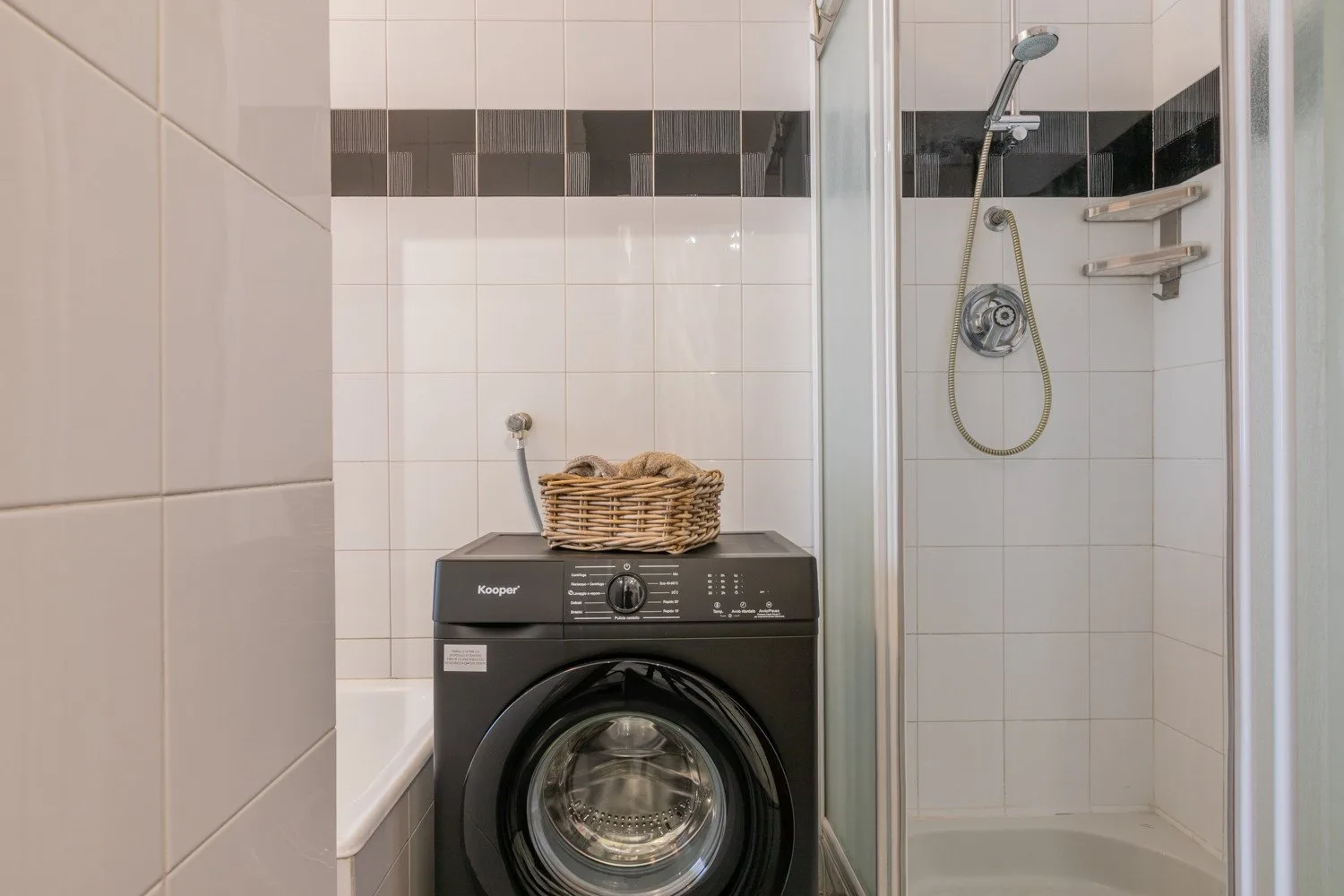 A tiled bathroom with a washing machine beside a glass-enclosed shower.