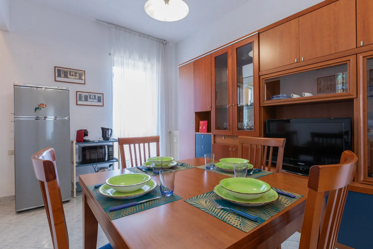 A dining area with a wooden table set with green plates beside a built-in cabinet.