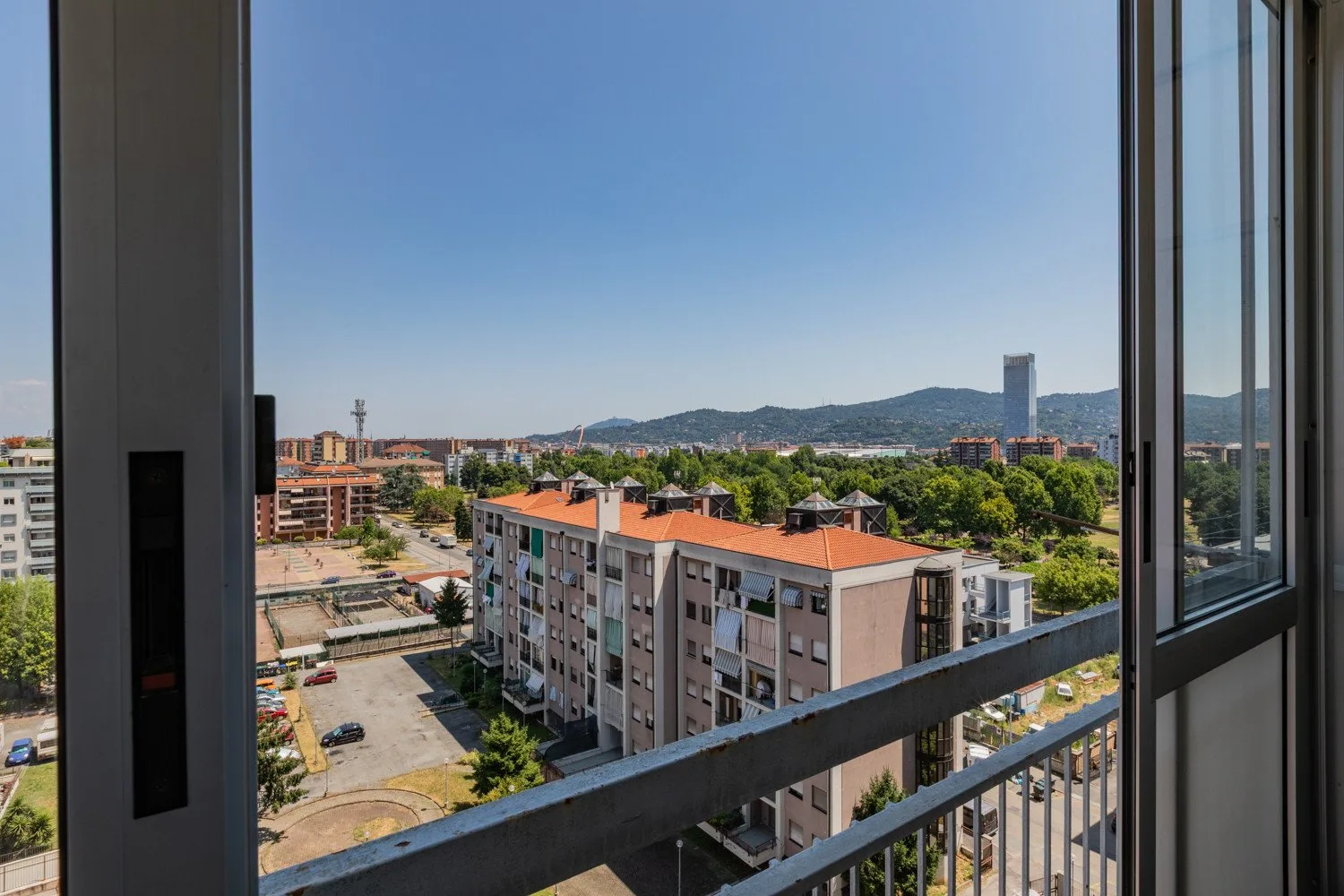 A cityscape viewed from a balcony, with apartment buildings and distant hills.