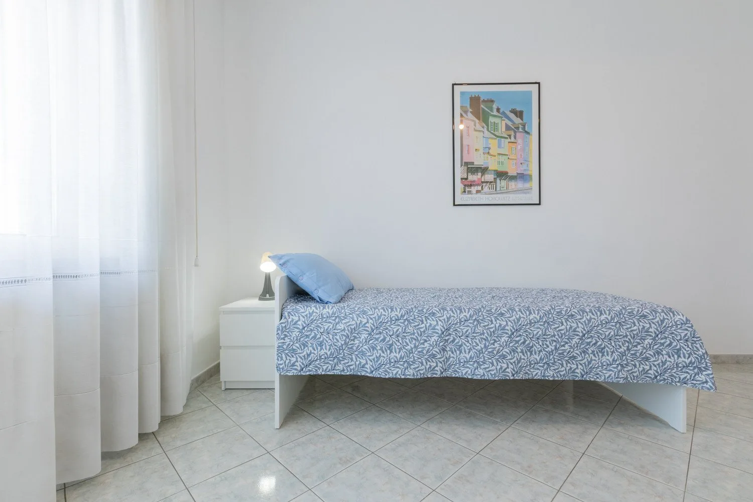 A bedroom with a single bed covered in a blue patterned bedspread.