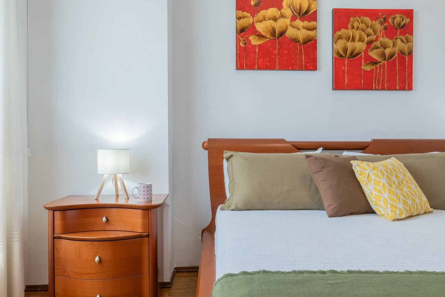 A bedroom with a wooden bed, colorful pillows, and floral artwork above it.