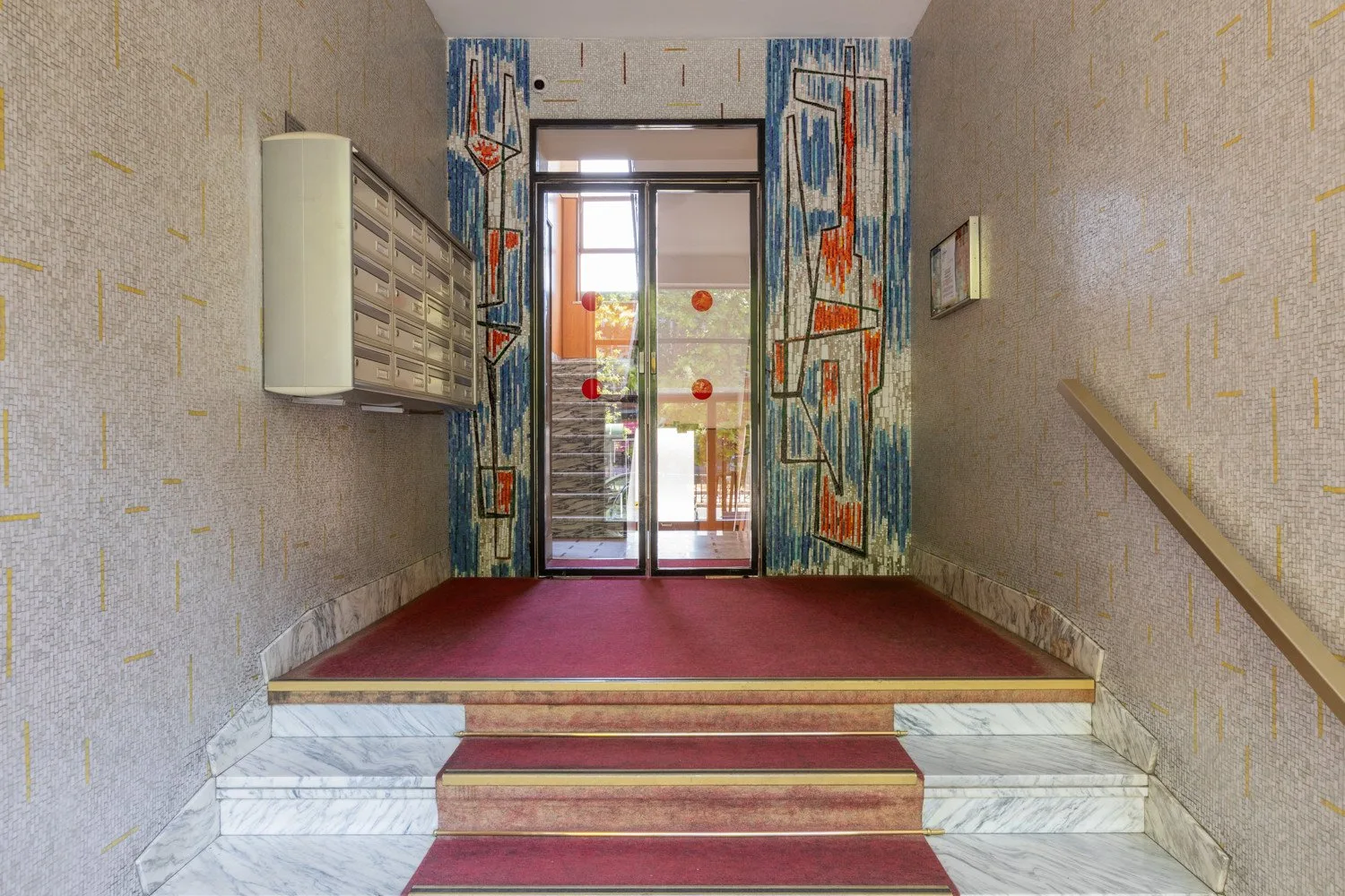 An interior stair landing with red carpet and colorful panels around a glass doorway.