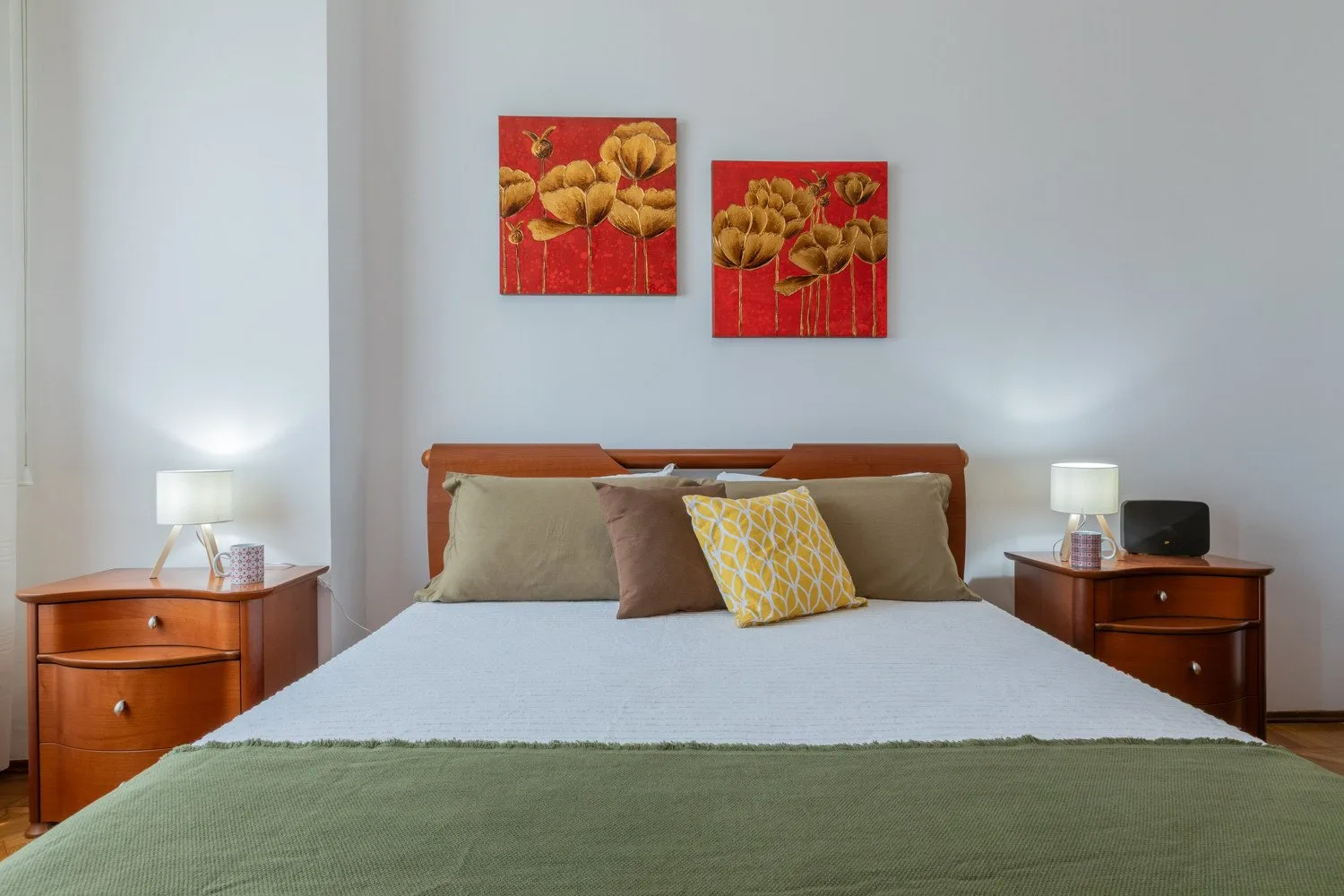 A bedroom with a neatly made bed and two colorful floral paintings above it.