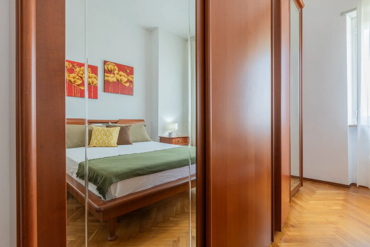 A bedroom with a bed, framed artwork, and mirrored wardrobe doors.