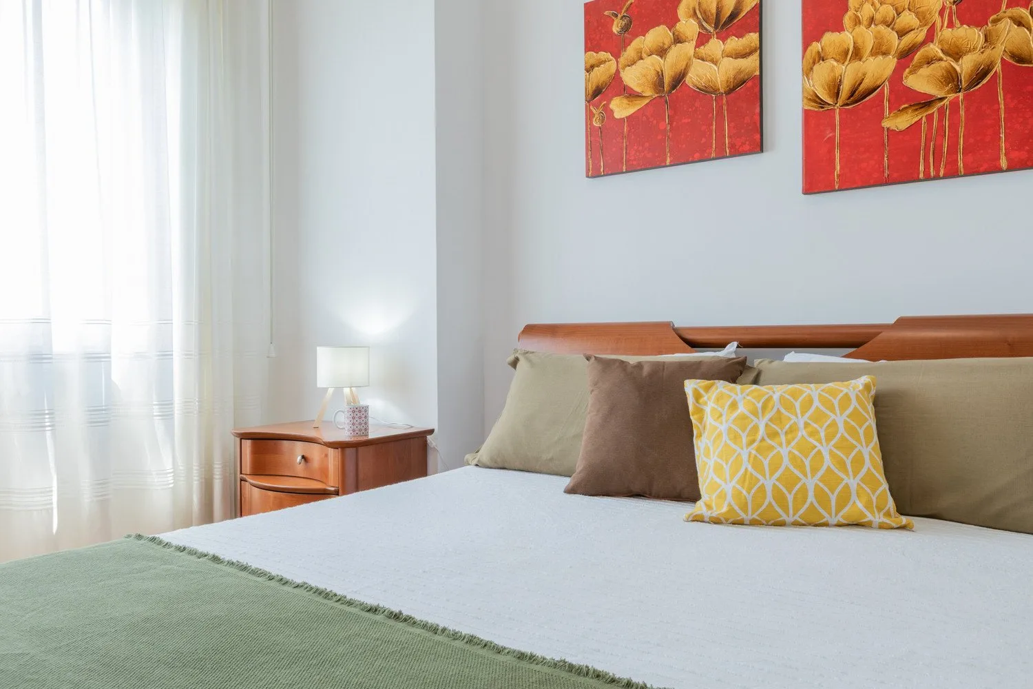 A bright bedroom with a neatly made bed and colorful floral artwork above it.