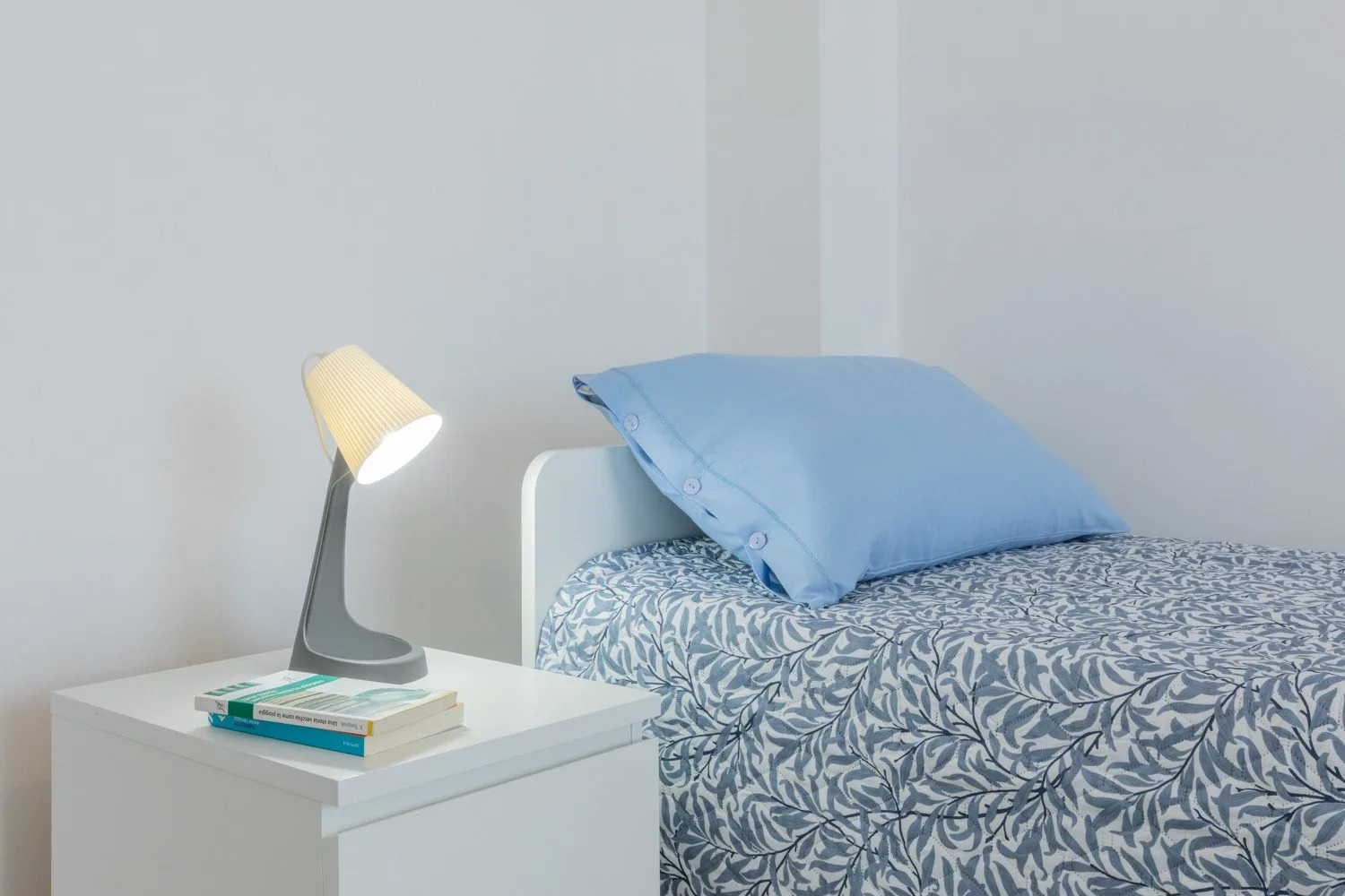 A bedroom with a bed, blue pillow, and bedside lamp.