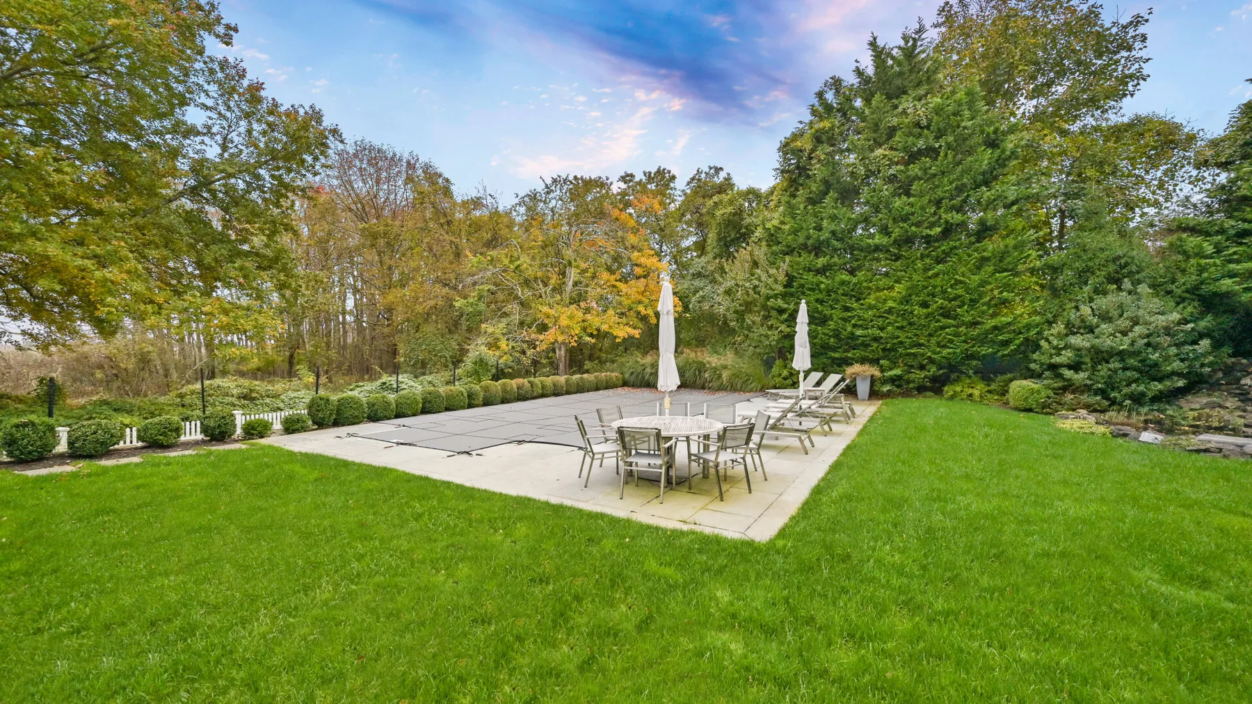 Un patio al aire libre con mesas y sillas junto a un amplio césped verde.