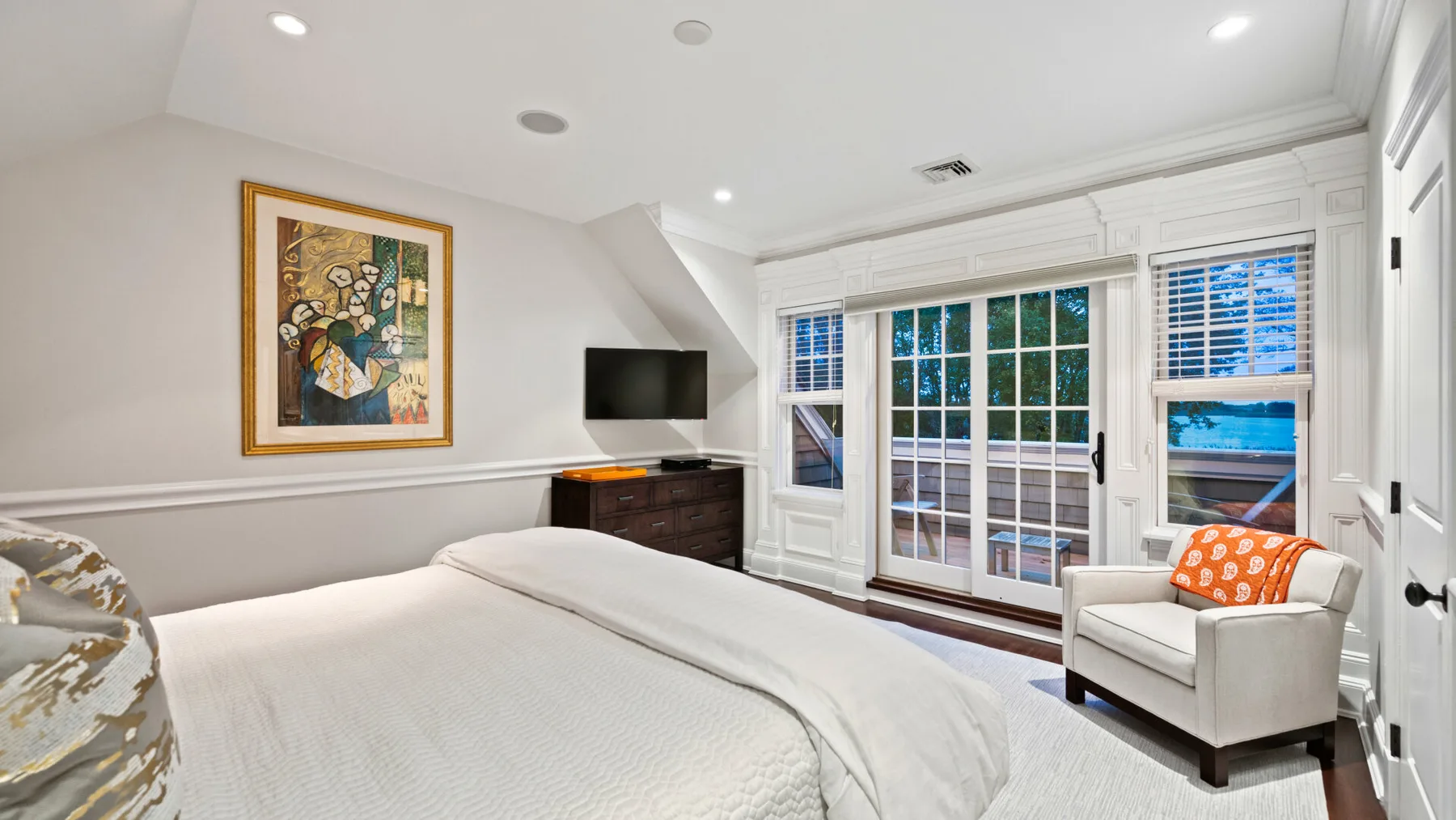 Un dormitorio luminoso con una cama bien tendida y ventanas a lo largo de una pared.