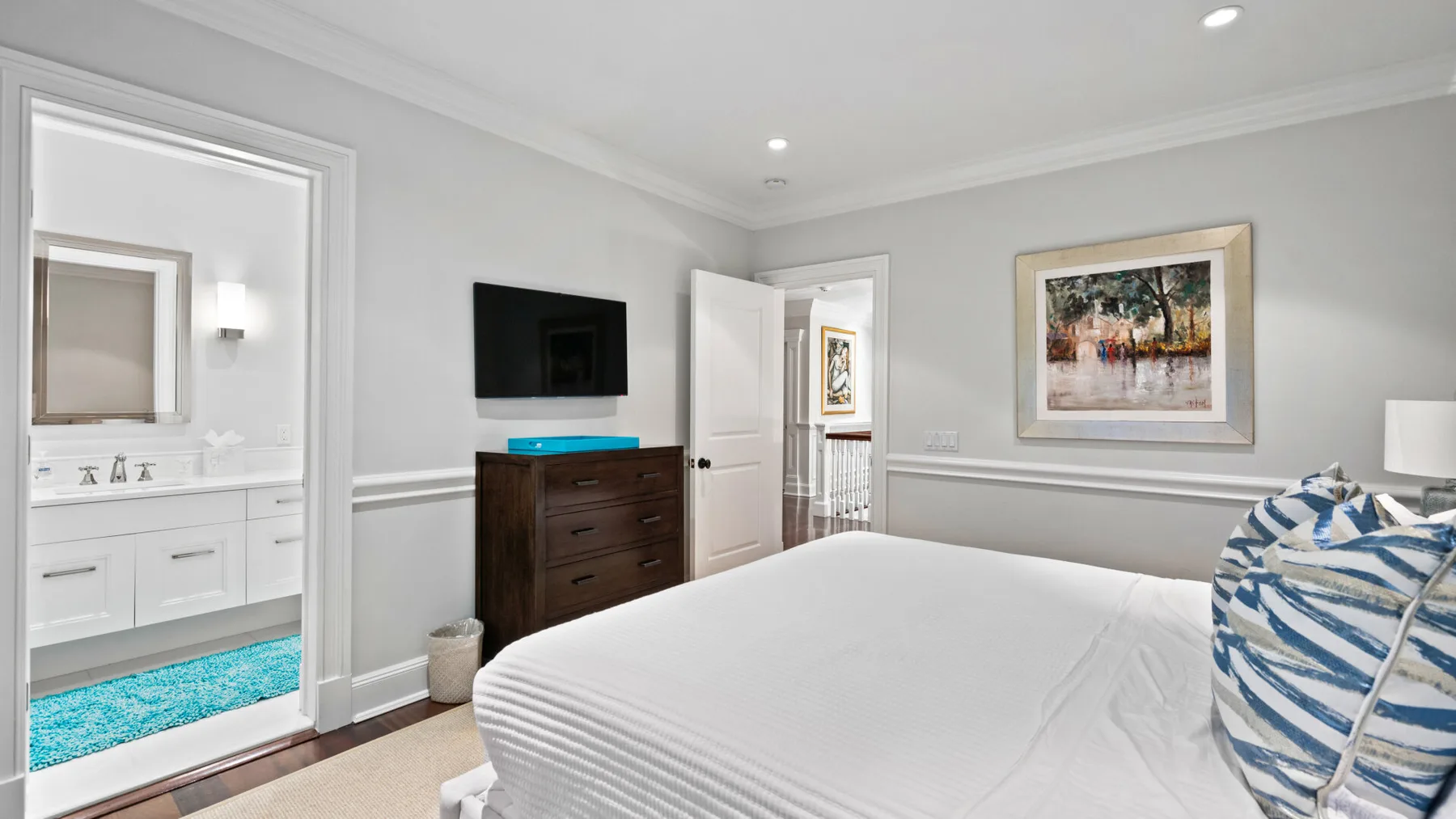 Un dormitorio con una cama bien tendida, una cómoda y un televisor en la pared.