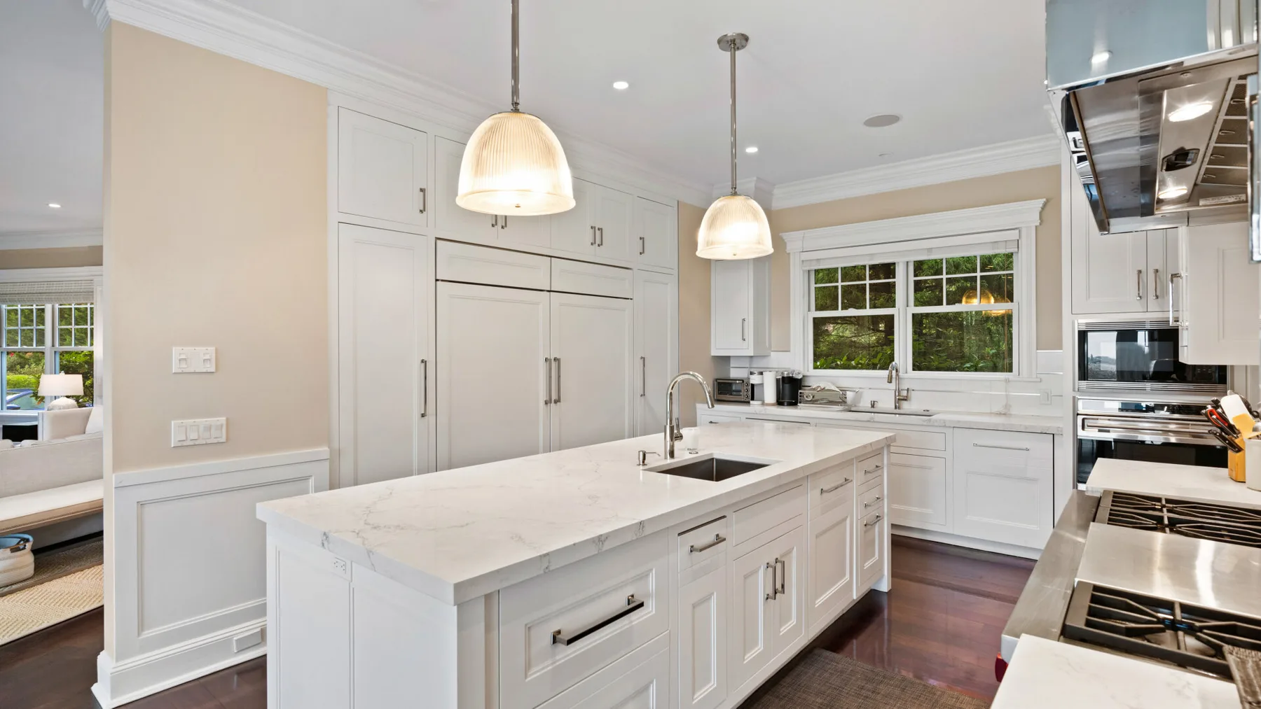 Una cocina luminosa con gabinetes blancos, una isla central y ventanas grandes.