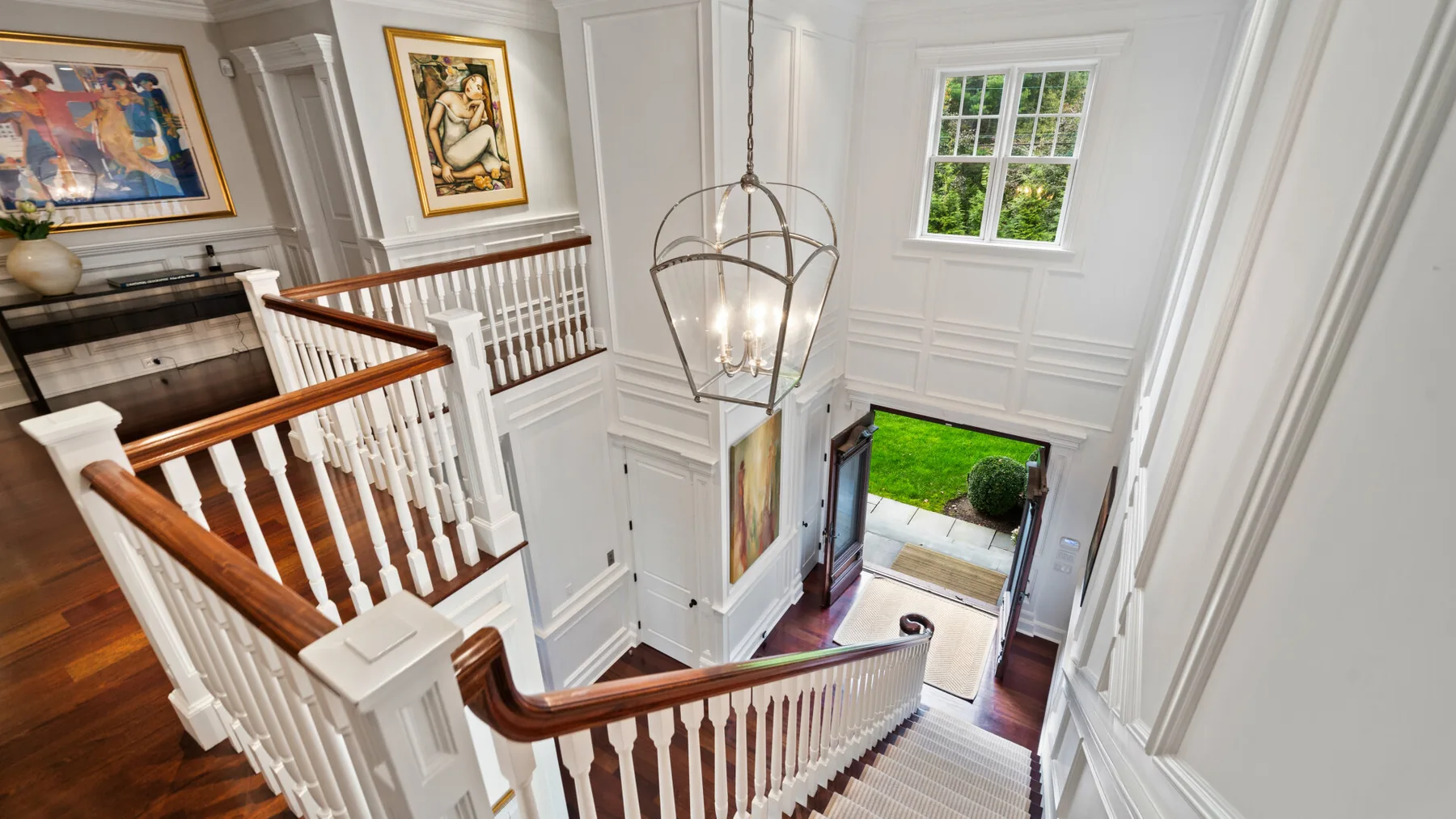 Una luminosa escalera interior blanca con cuadros enmarcados y una lámpara colgante.