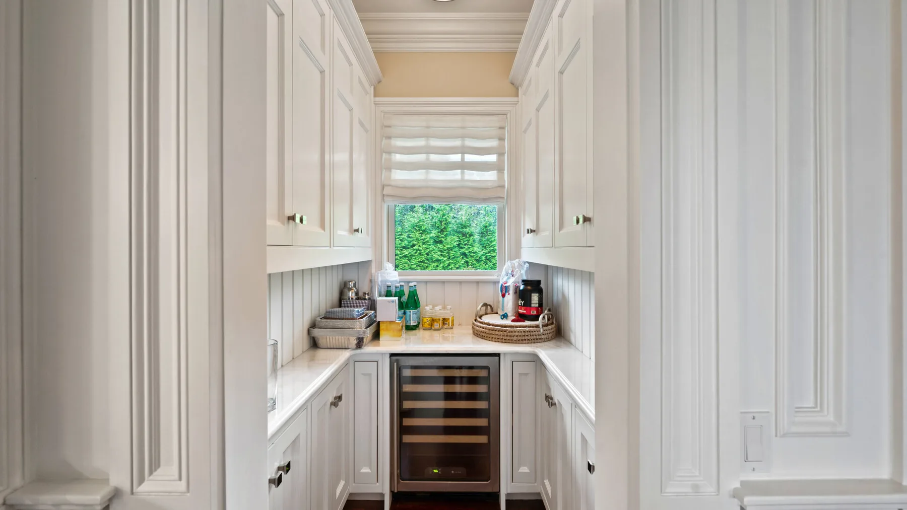 Un rincón de cocina luminoso con gabinetes blancos, una ventana y una nevera para bebidas.