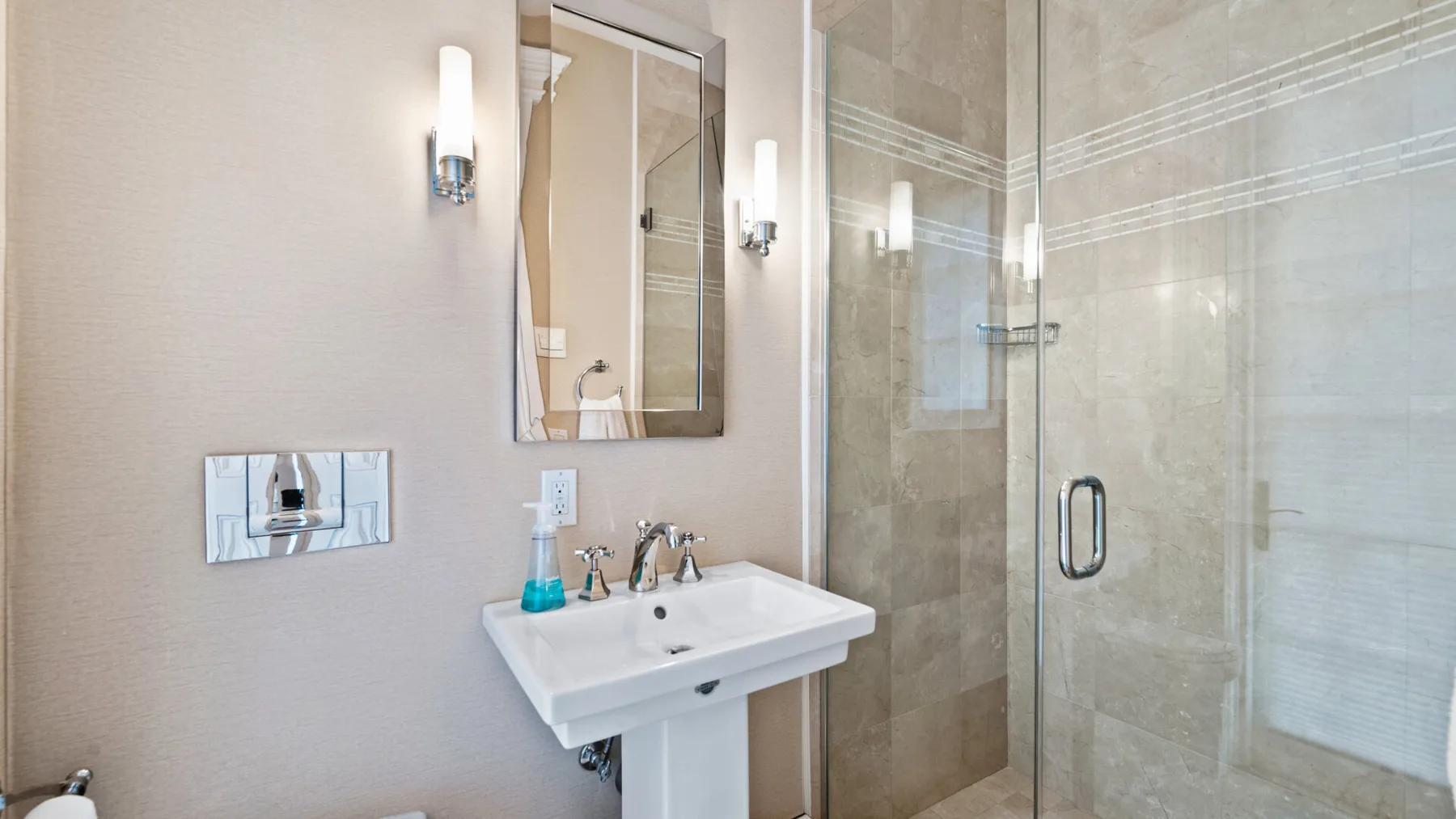 Un baño con lavabo de pedestal, espejo y ducha de vidrio.