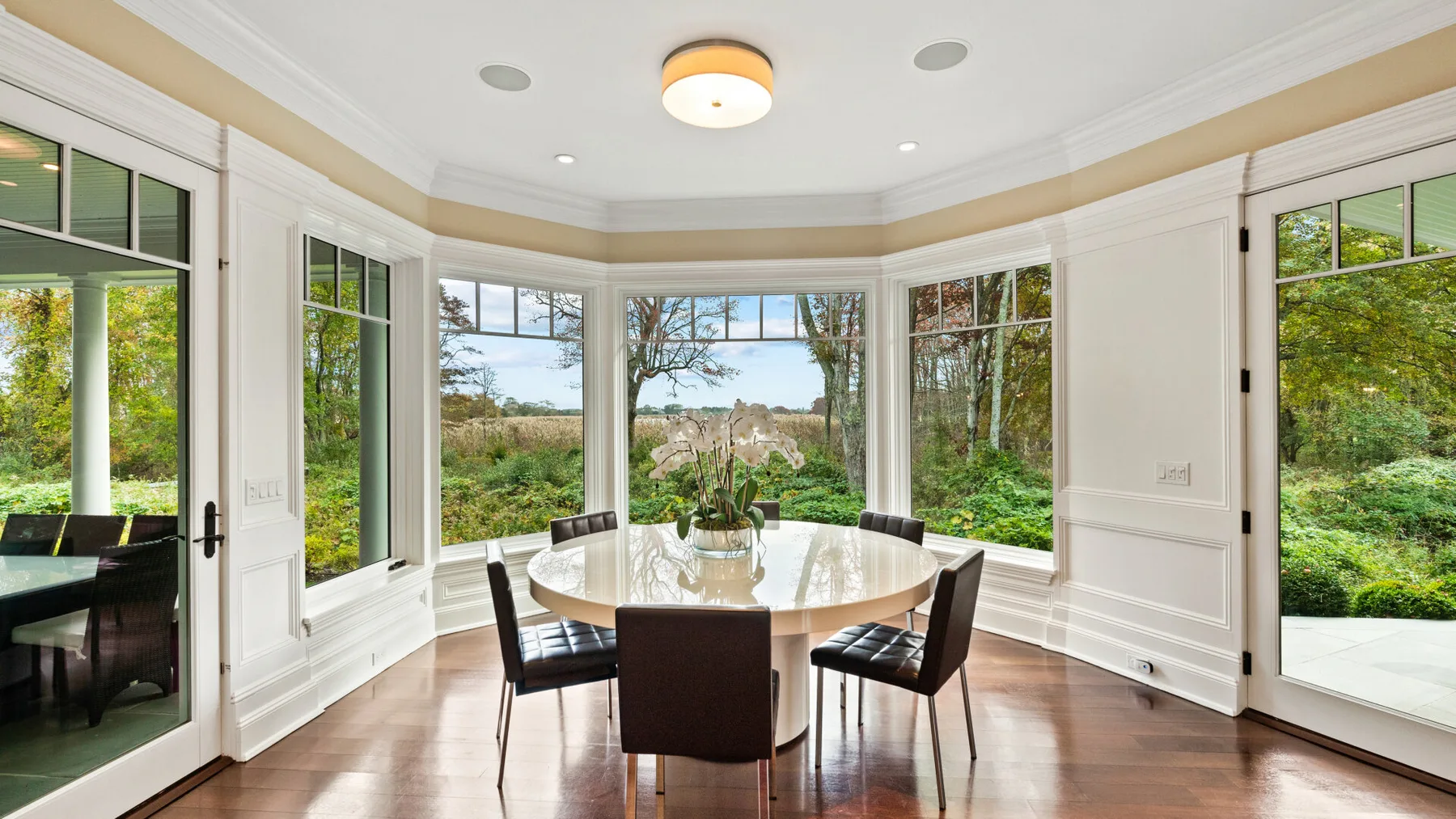Un comedor luminoso con una mesa y sillas junto a grandes ventanas con vistas a la vegetación.