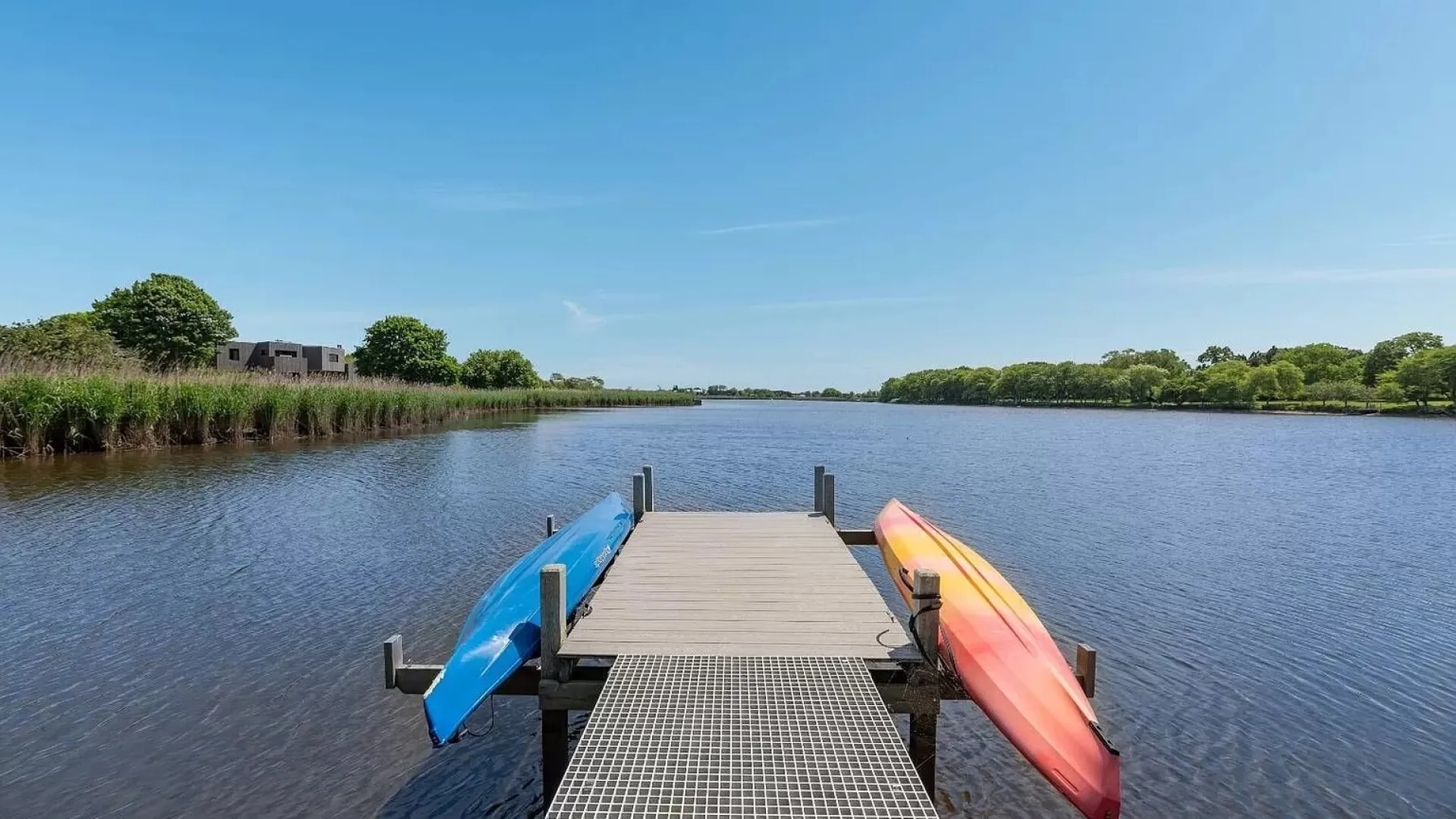 Un muelle de madera se adentra en un lago, con kayaks de colores a los lados.