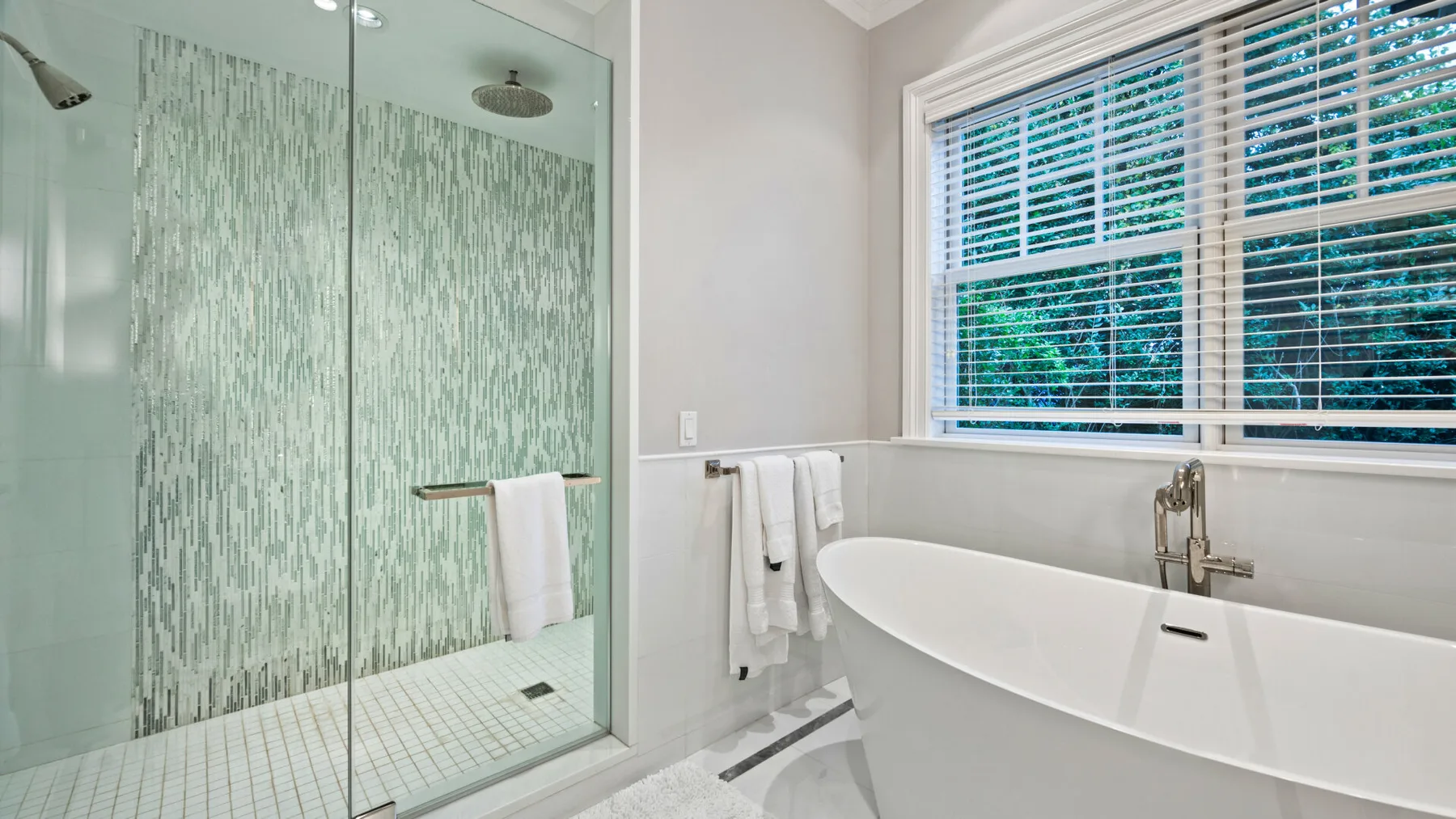 Un baño luminoso con una bañera independiente junto a una ducha de vidrio.