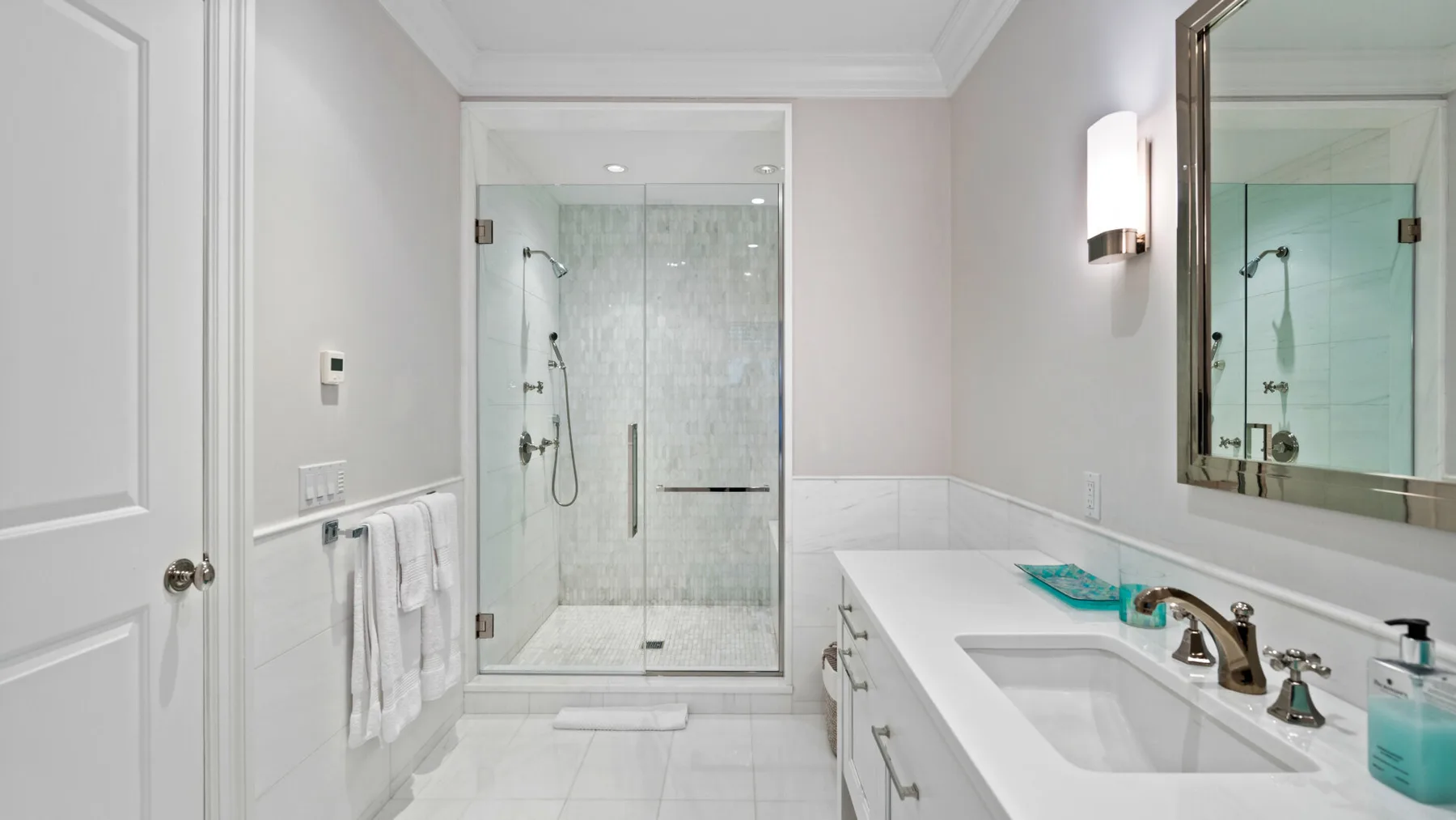Un baño luminoso con ducha de vidrio y un largo tocador.