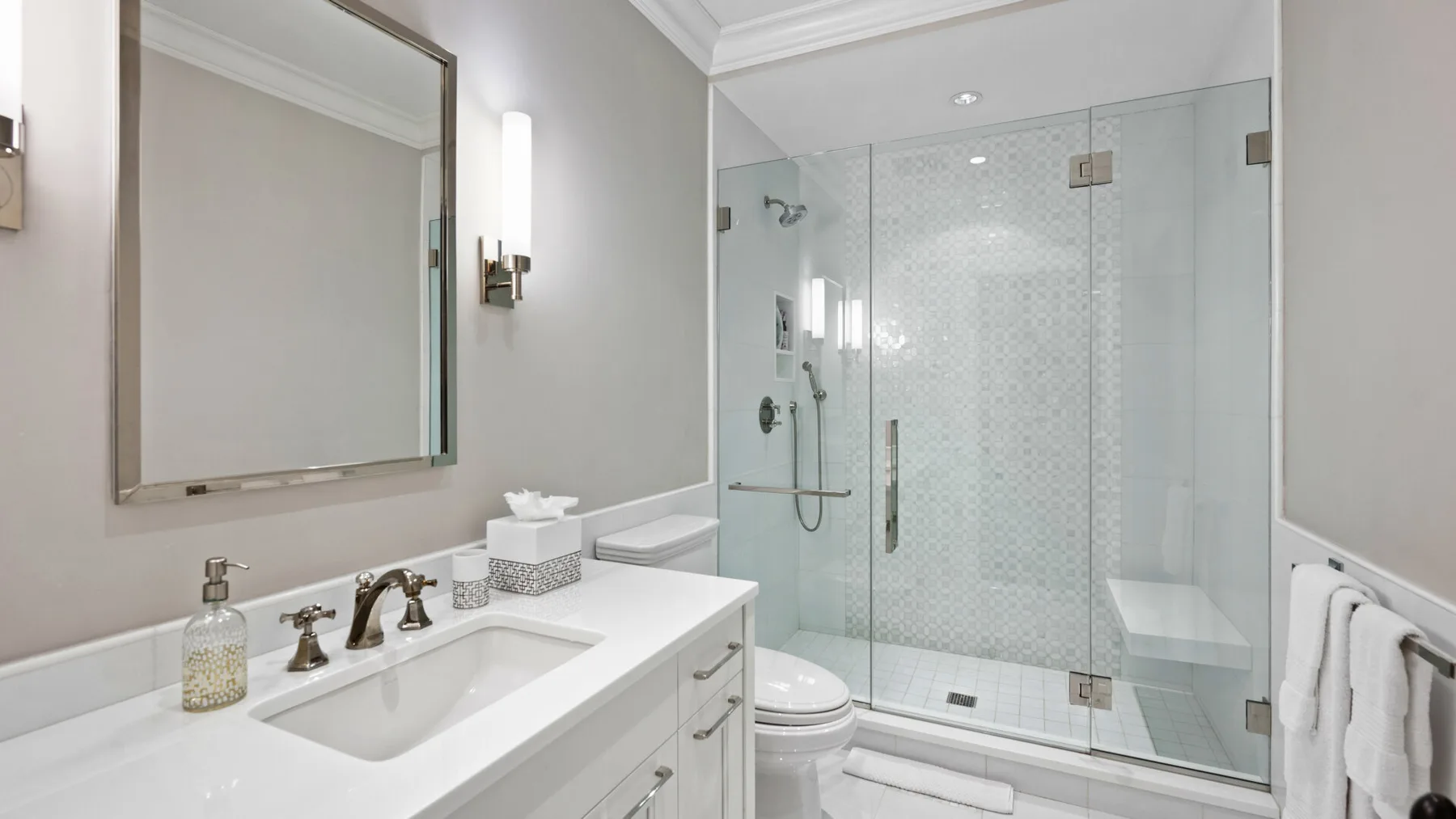 Un baño luminoso con lavabo, espejo y ducha de vidrio.